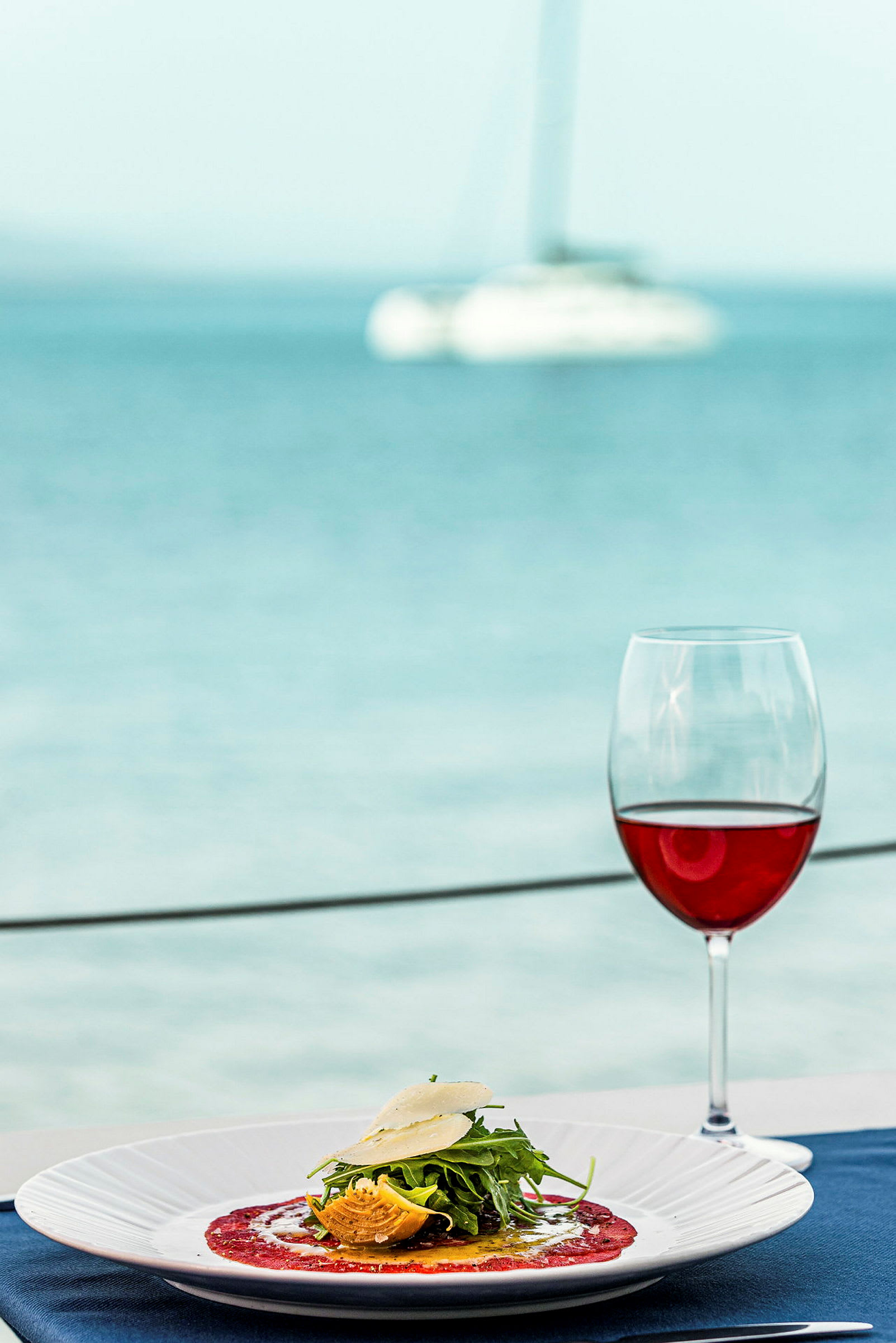 En tallerken med mad og et glas rødvin ved havet. (AI-genereret tekst)