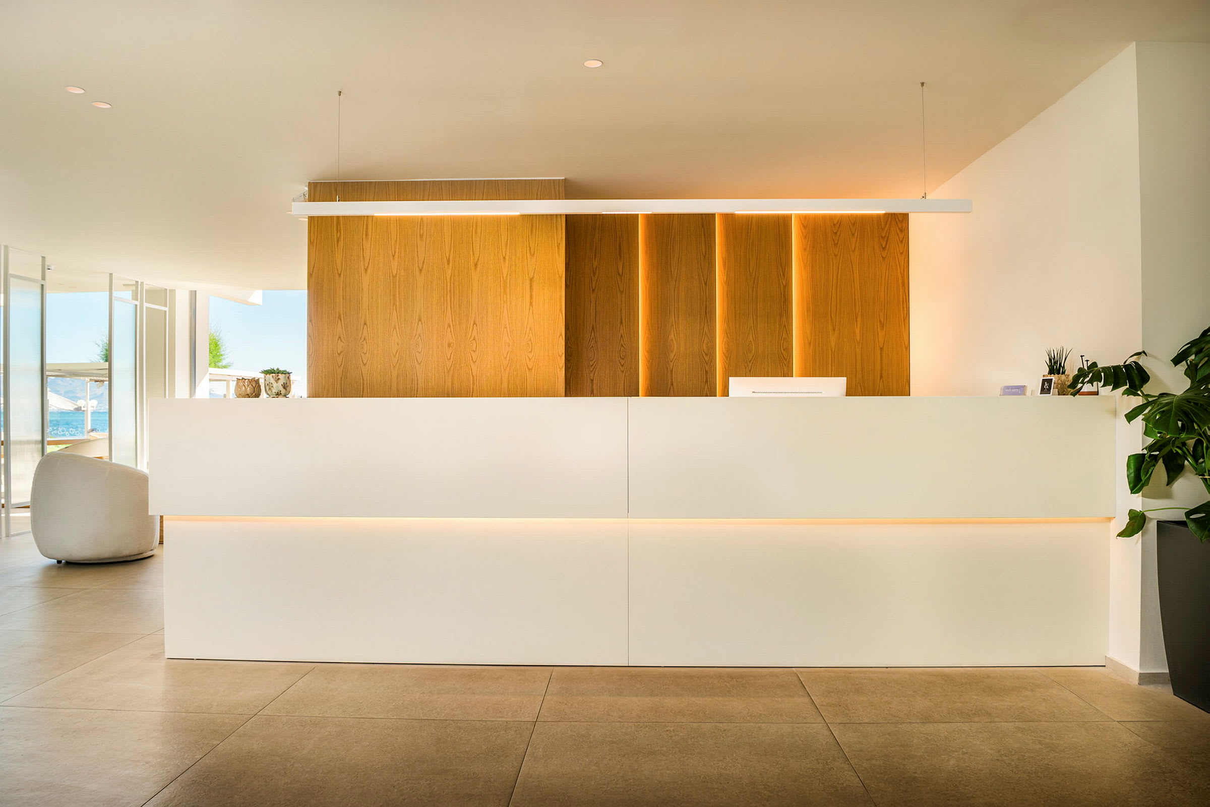Billede af en reception med moderne design. Baggrunden består af træpaneler, og disken er hvid. Planter ses til højre. (AI-genereret tekst)