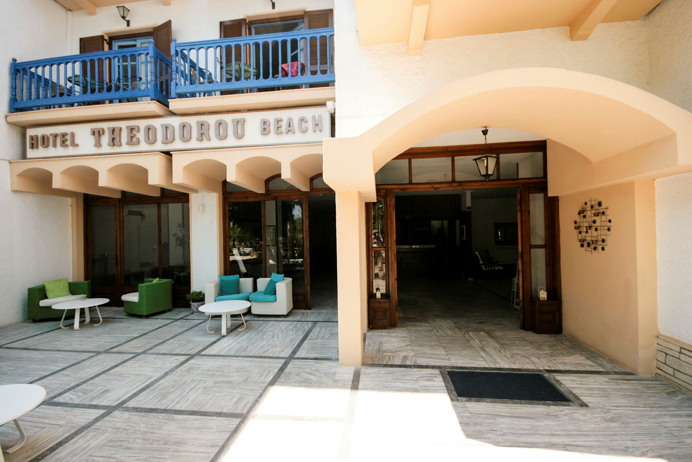 Indgang til Hotel Theodoru Beach med siddeområder udenfor. (AI-genereret tekst)