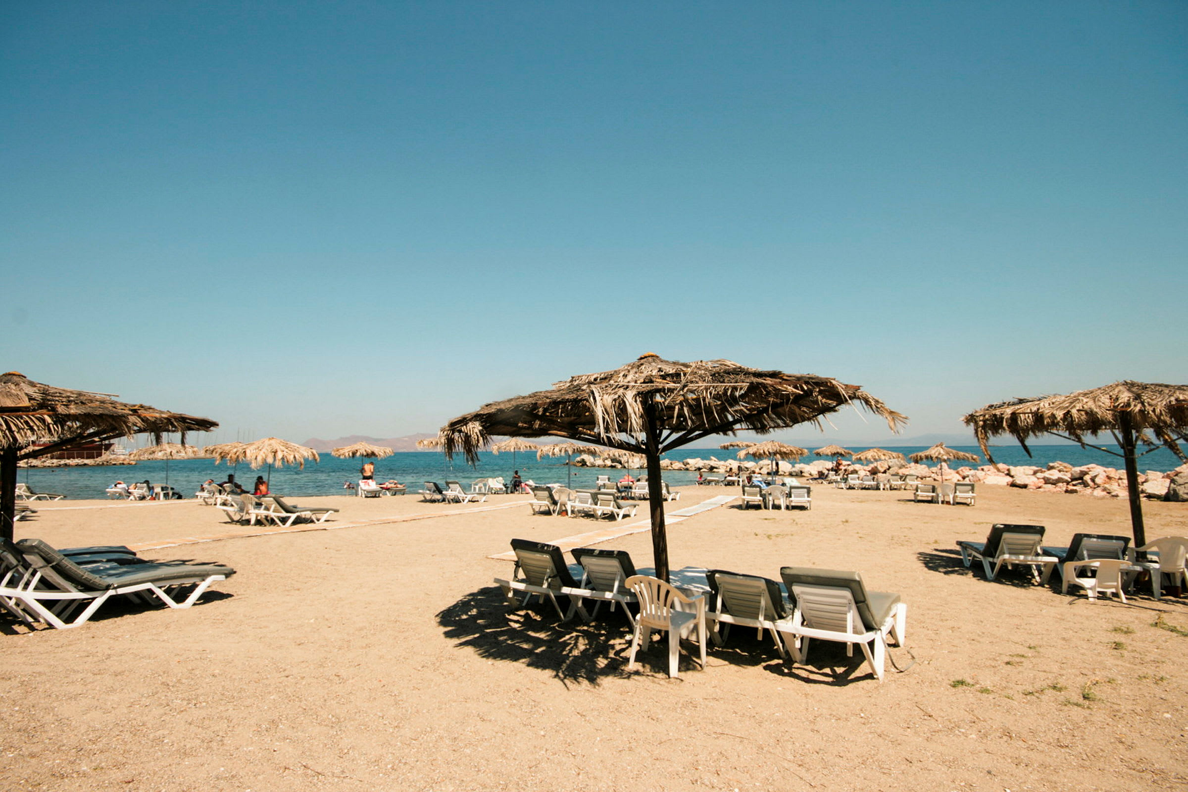 Strand med liggestole og parasoller med stråtag. (AI-genereret tekst)