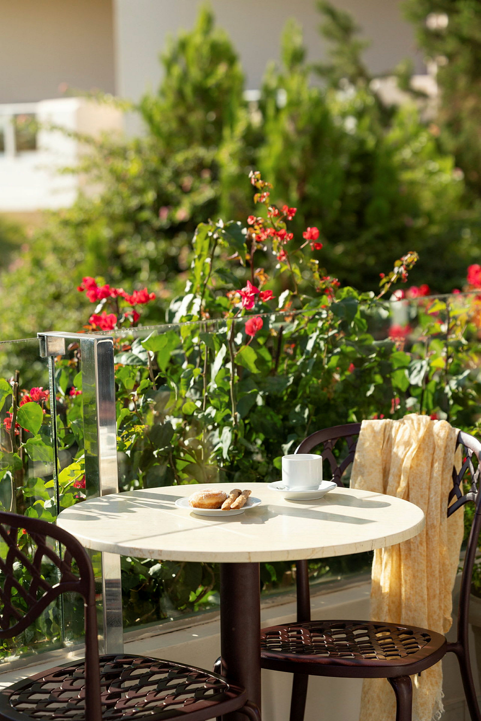 Bord med kaffekop, bagværk og stole på terrasse med en frodig omgivelser. (AI-genereret tekst)
