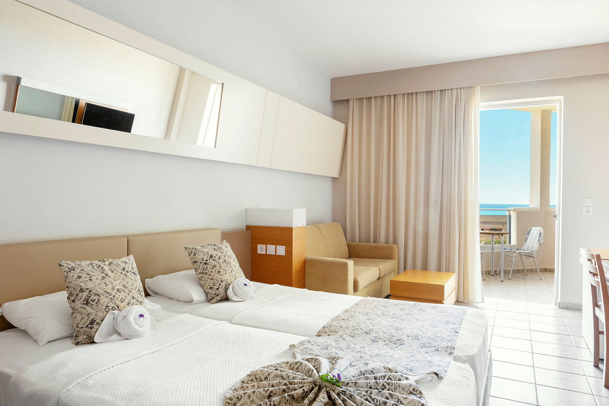 Et hotelværelse med to enkeltsenge, en sofa, et bord og en altan med udsigt til havet. (AI-genereret tekst)