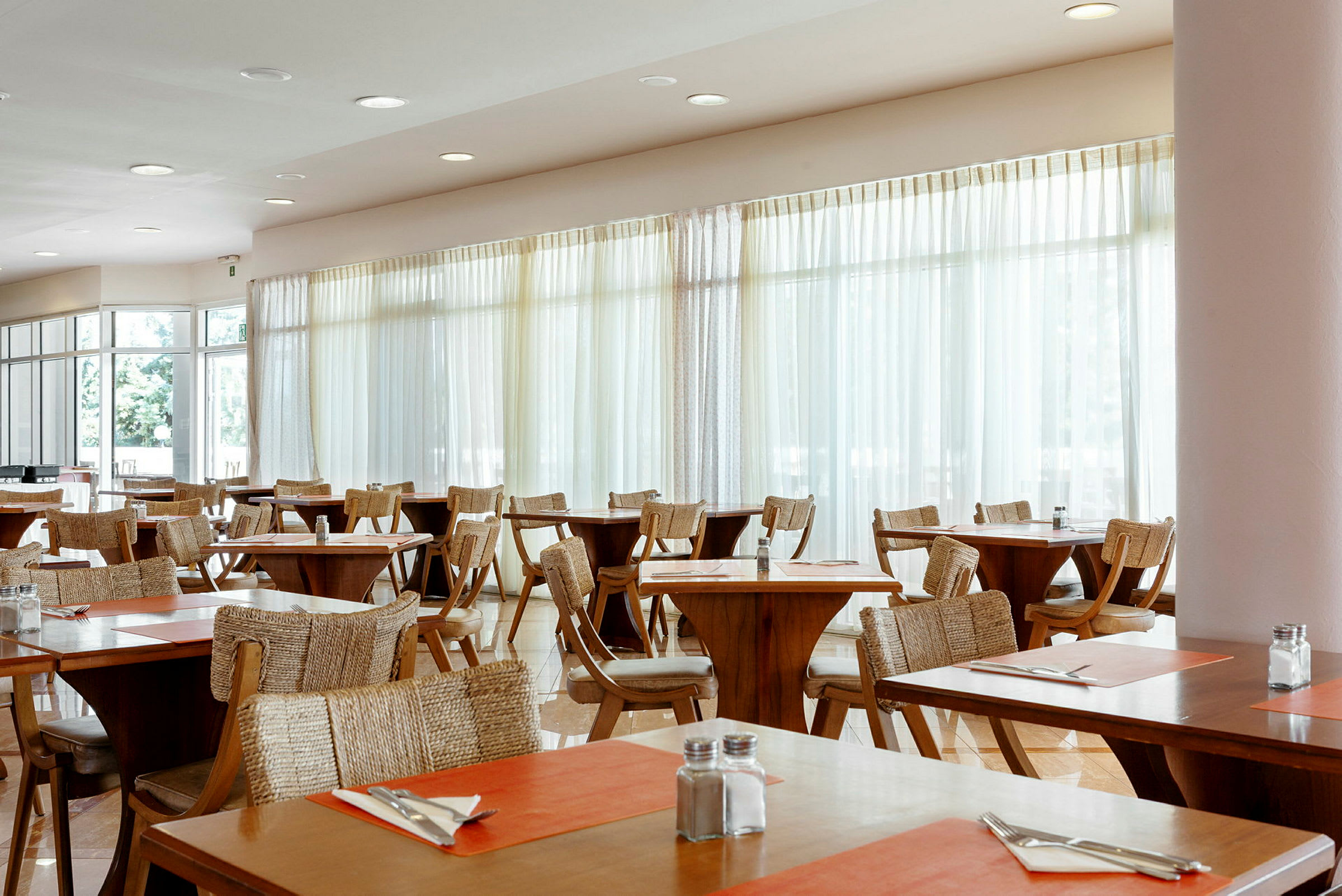 En restaurant med træborde og stole, dekoreret med orange bordunderlag og opstillet bestik. (AI-genereret tekst)