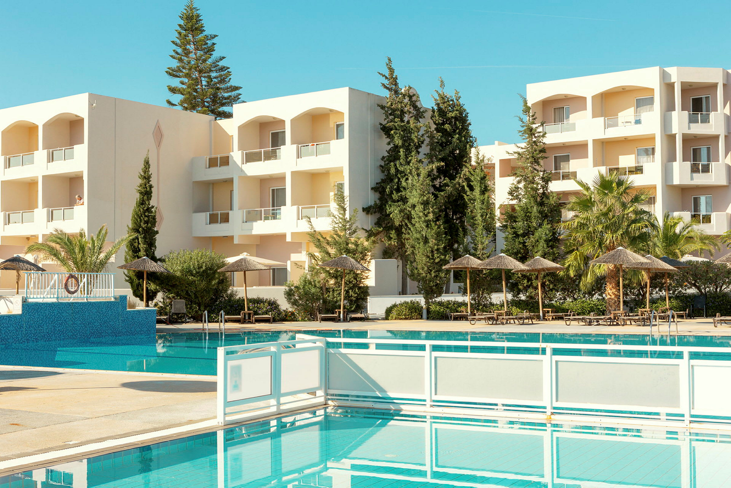 Hotelbygning med altaner, omgivet af grønne områder og udsigt til en pool. (AI-genereret tekst)