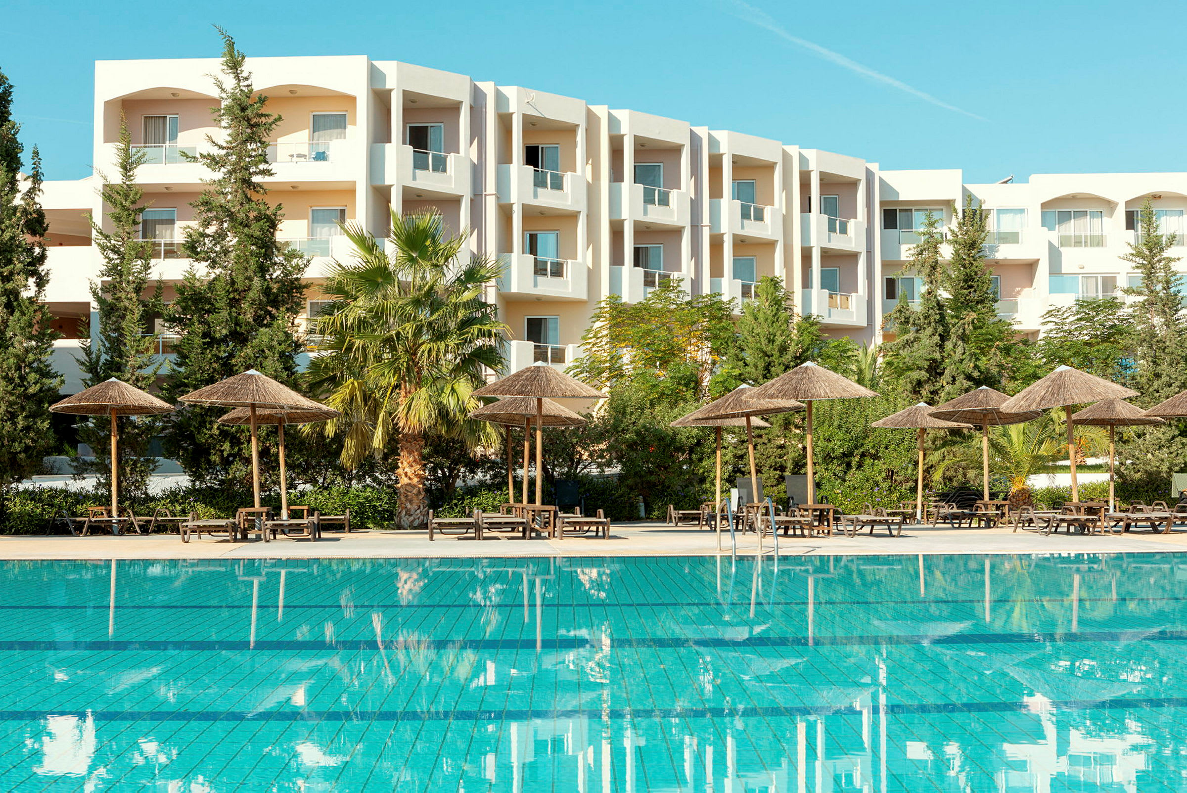 Udendørs swimmingpool med parasoller og en hvid bygning i baggrunden. (AI-genereret tekst)