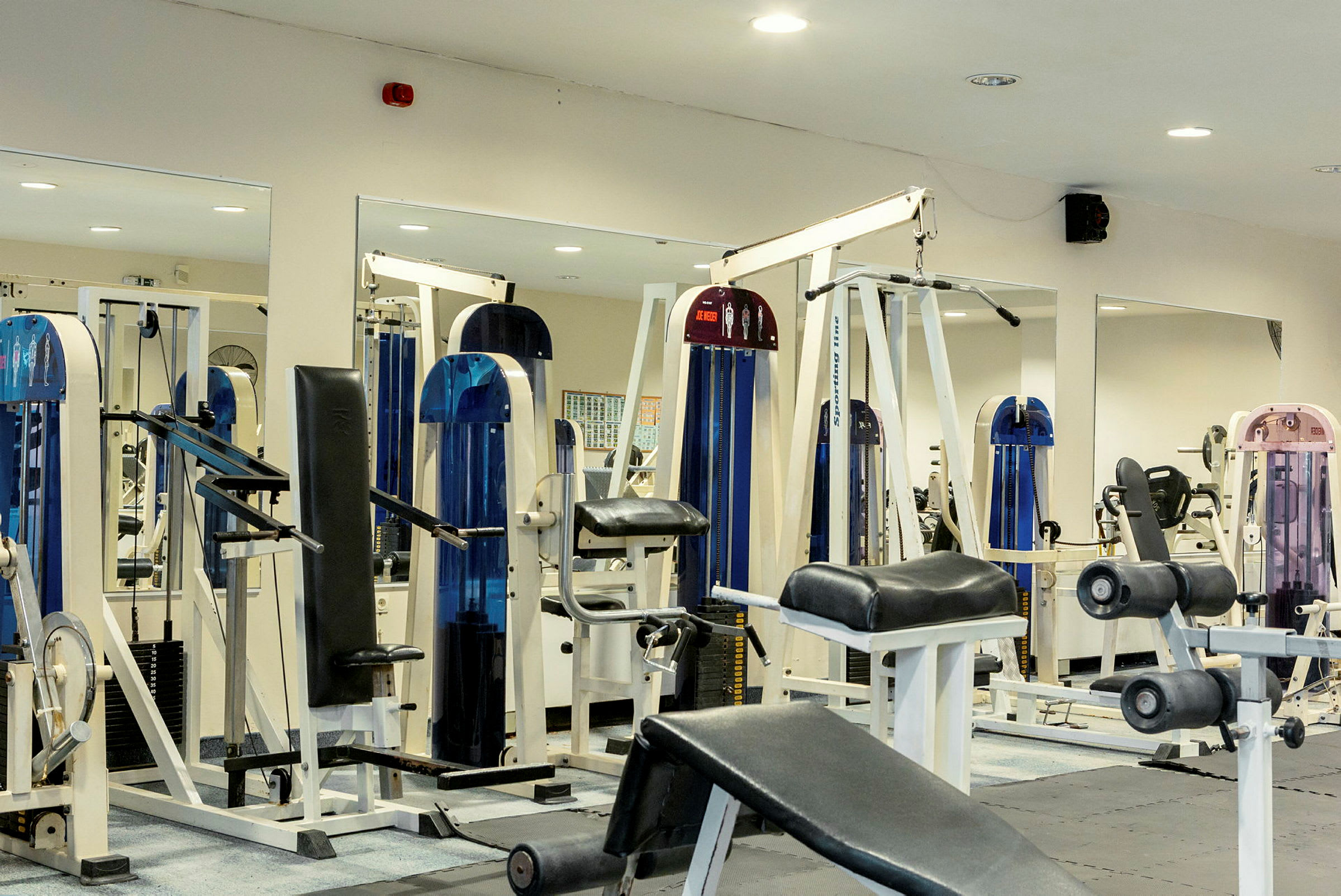 Billede af et fitnesscenter med forskellige træningsmaskiner og -udstyr. (AI-genereret tekst)