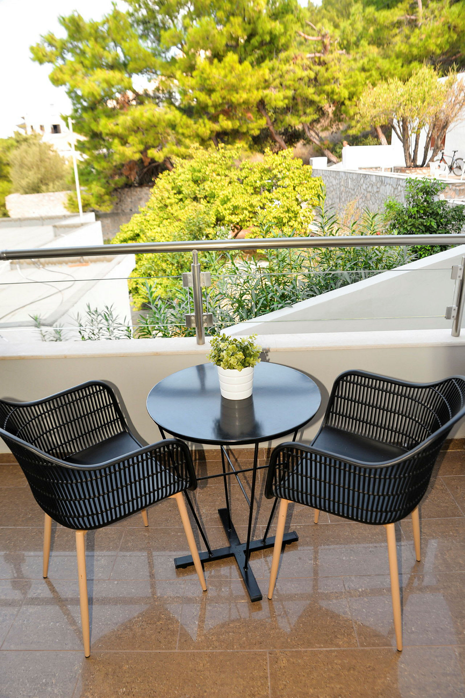 En terrasse med et bord og to stole foran et gelænder, omgivet af grønne træer. (AI-genereret tekst)