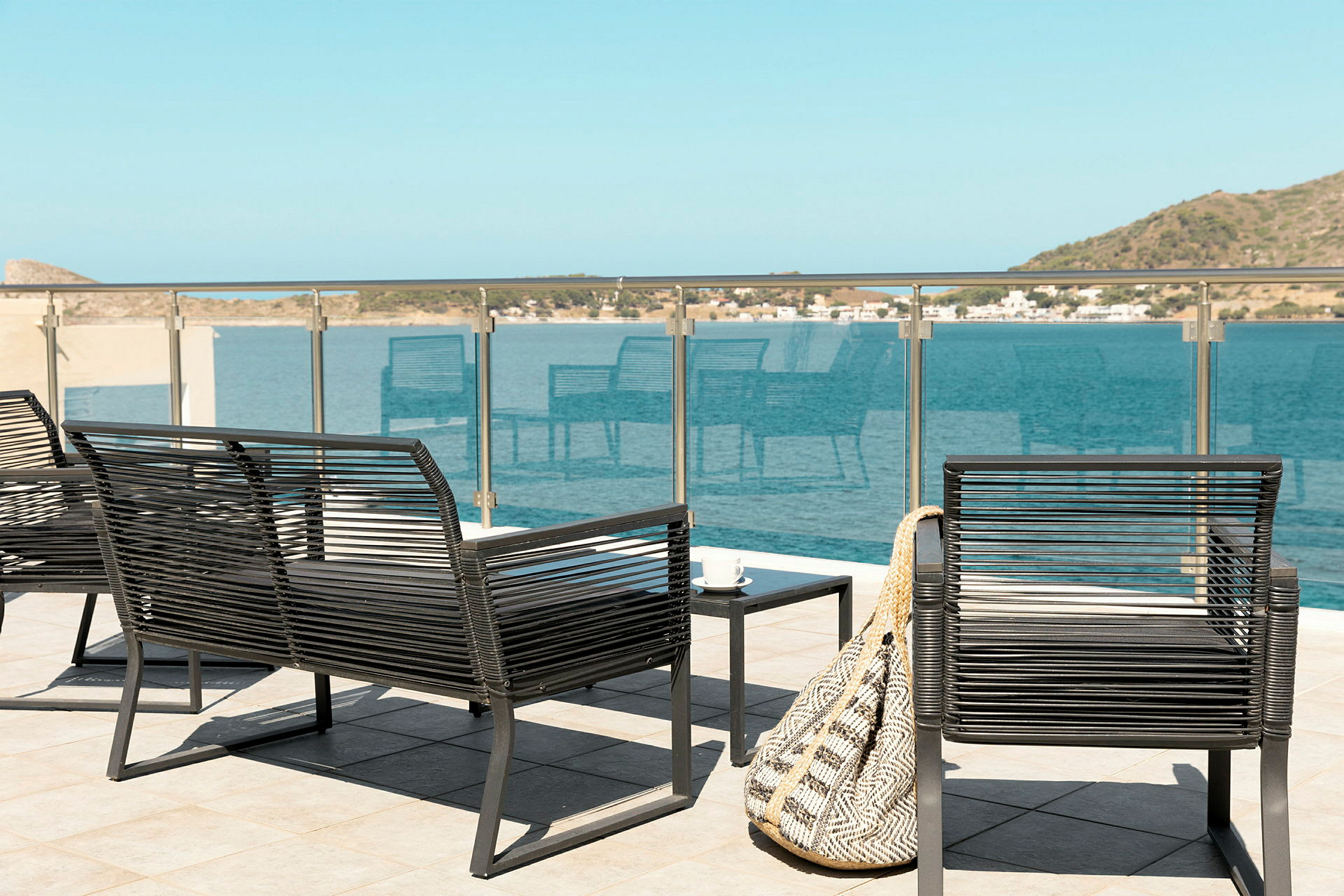 Udendørsmøbler på en terrasse med udsigt over havet og de omkringliggende omgivelser. (AI-genereret tekst)