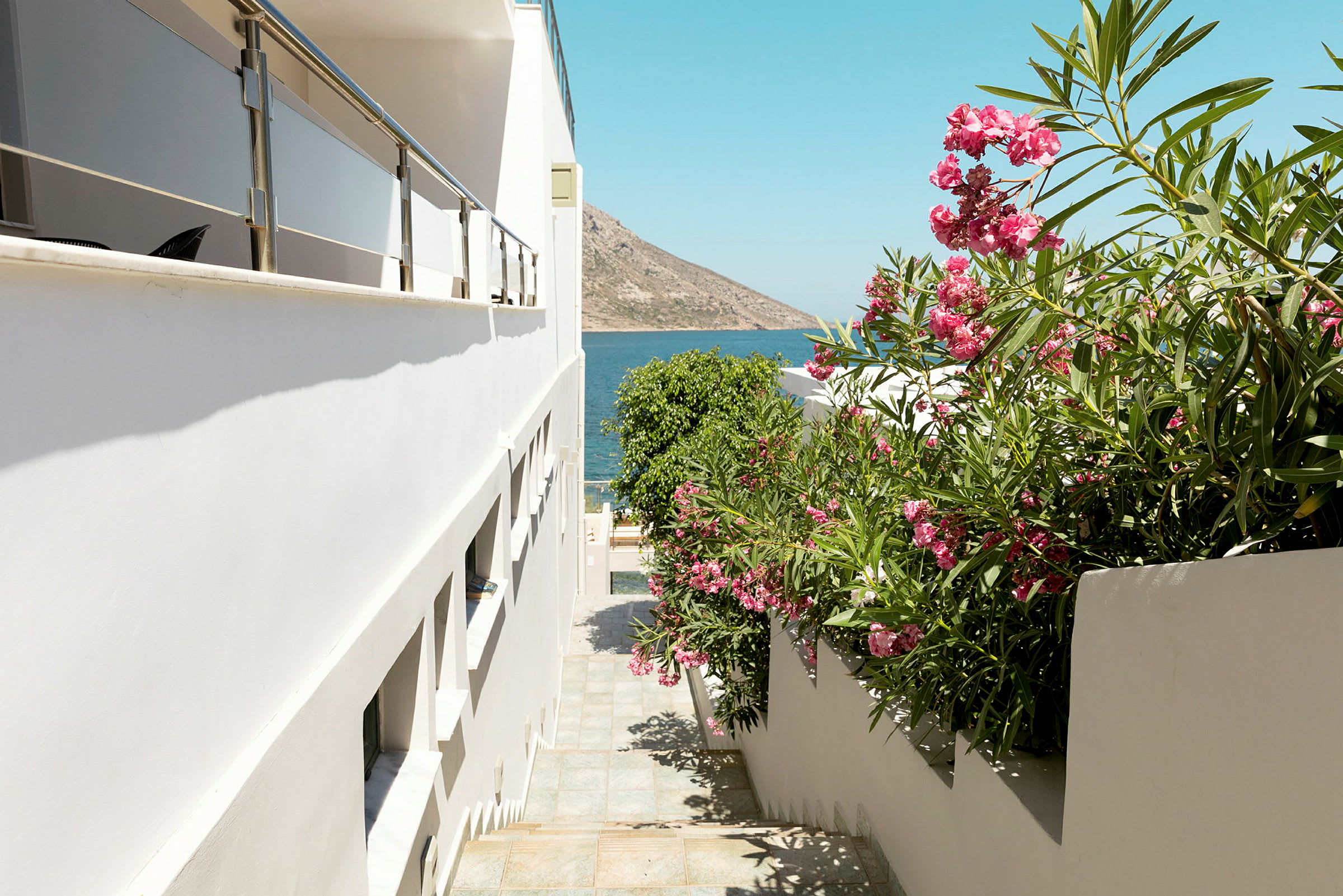 Hvid bygning med en trappe ned mod blomstrende vegetation og havet i baggrunden. (AI-genereret tekst)