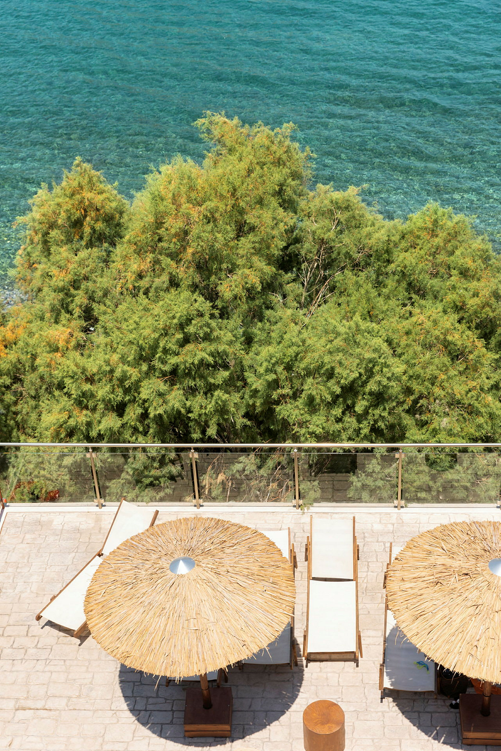 Strandstole og parasoller på en terrasse med udsigt over havet og grønne træer. (AI-genereret tekst)