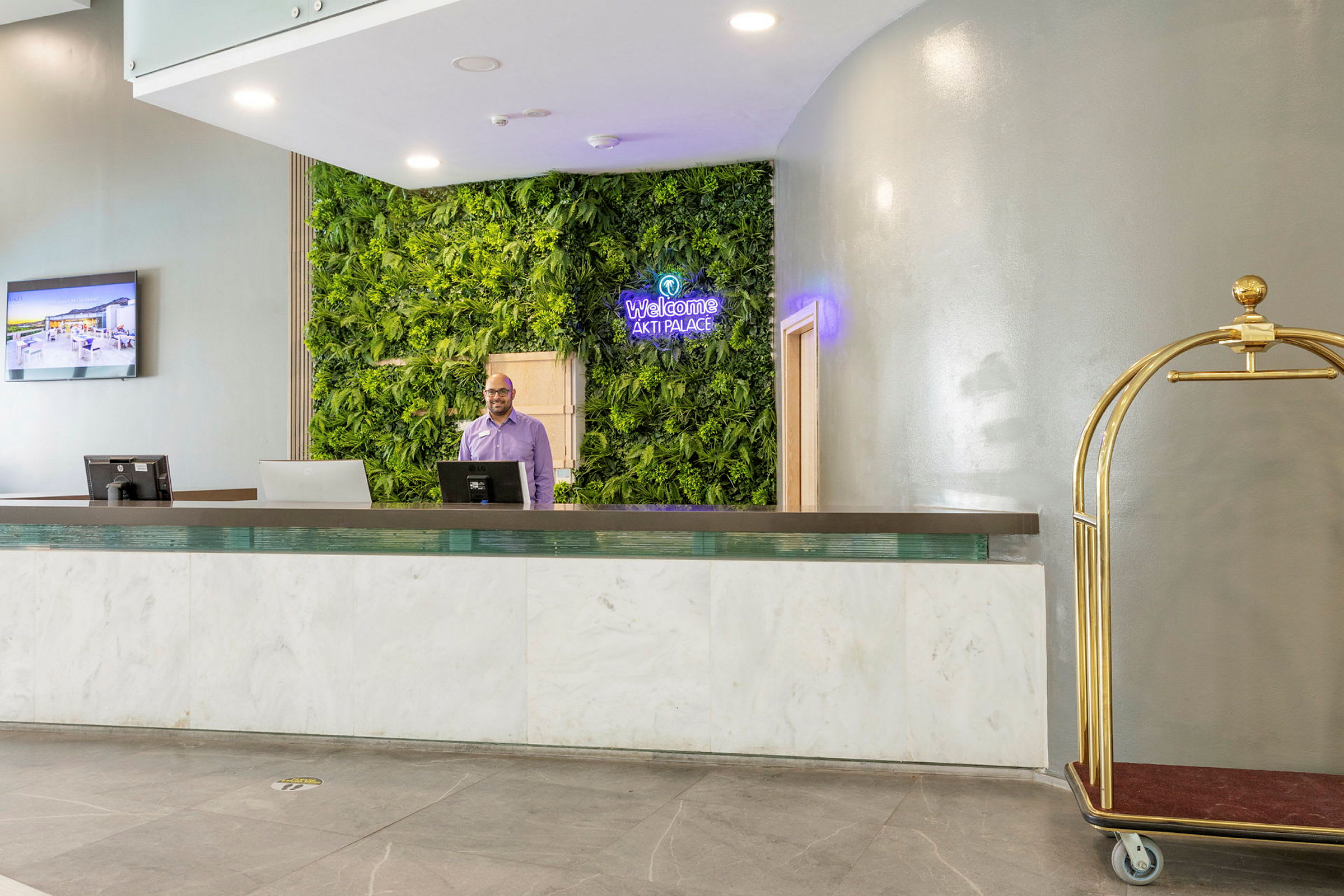 Hotelreception med væg dekoreret med grønne planter og en bagagevogn. (AI-genereret tekst)