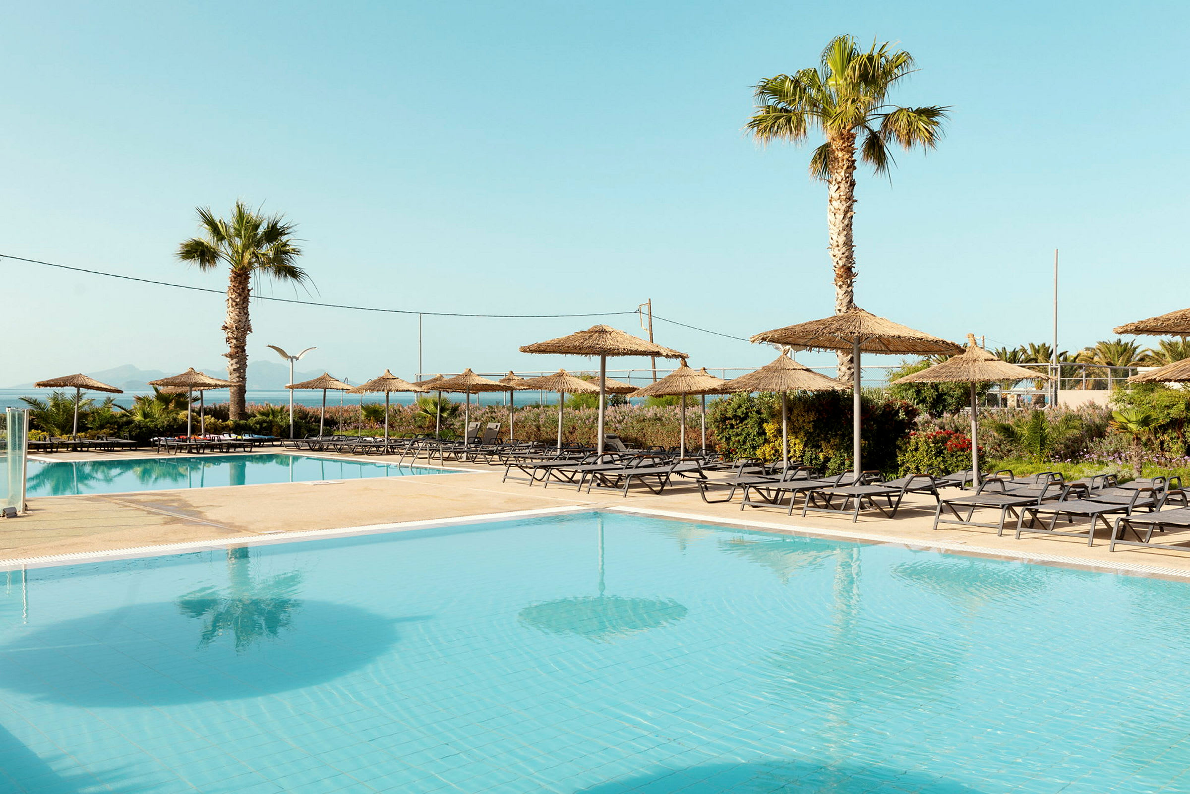 Billede af en pool med liggestole og parasoller i en hotelresort-omgivelser. (AI-genereret tekst)