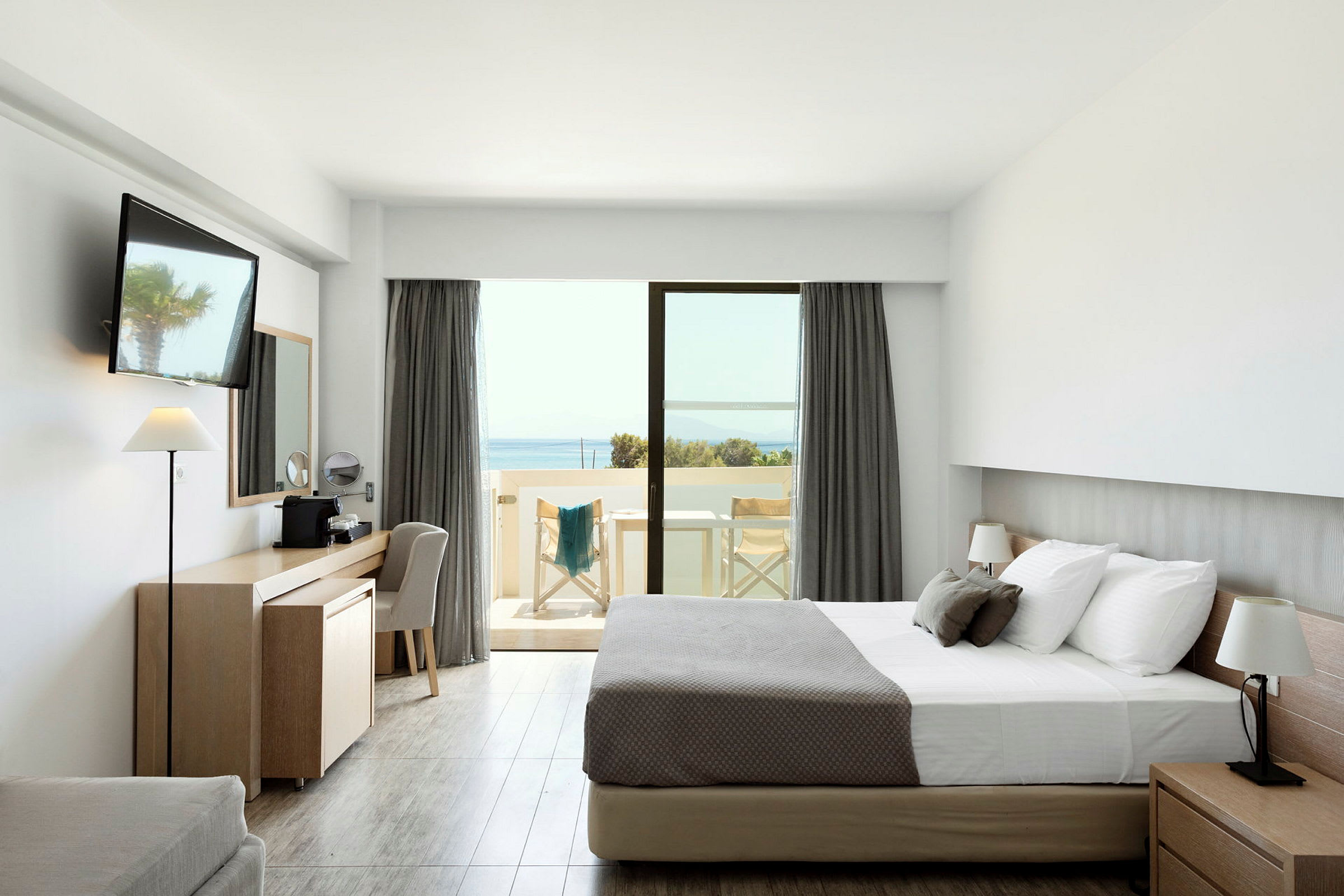 Et hotelværelse med en dobbeltseng, skrivebord og en balkon med udsigt over havet. (AI-genereret tekst)