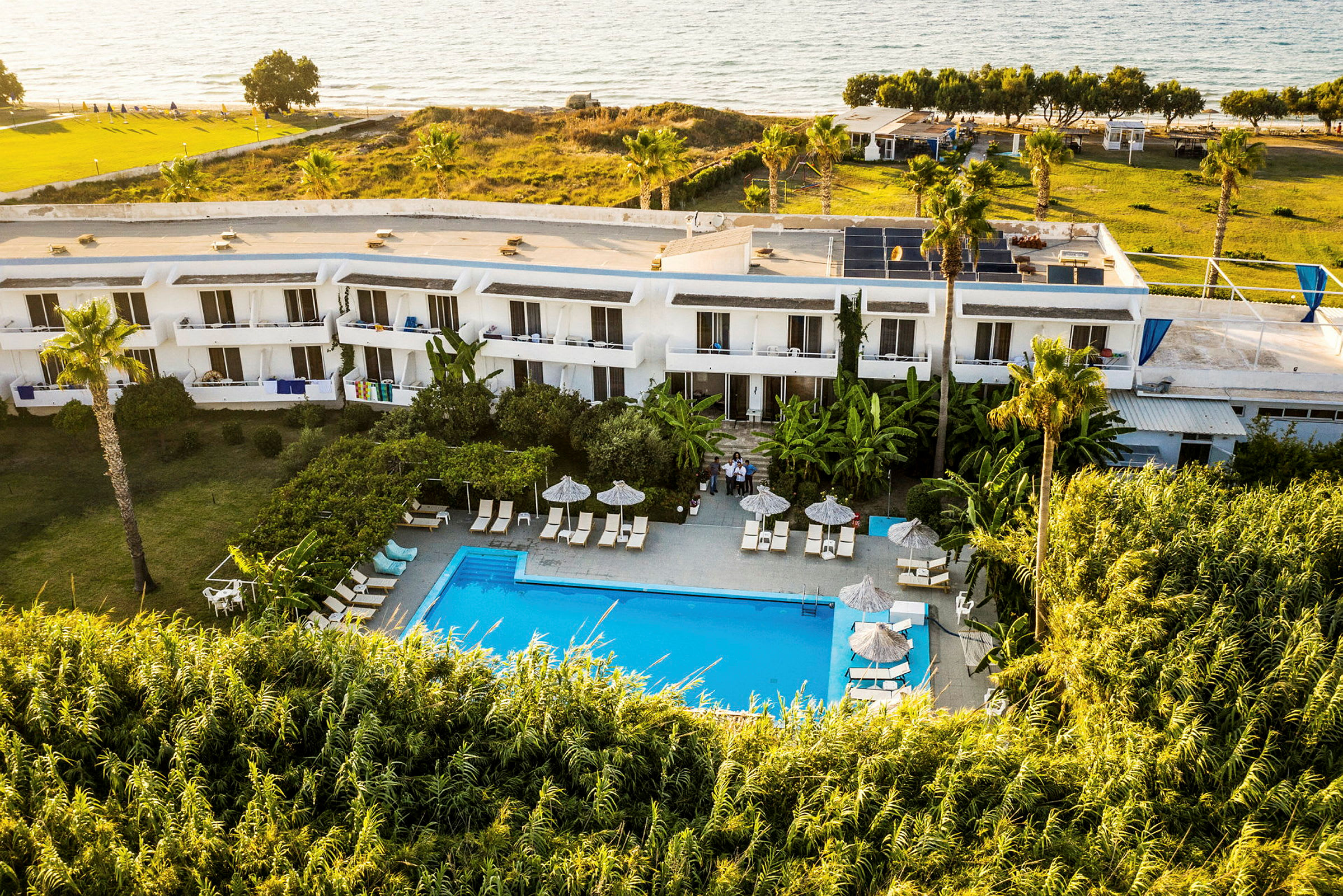 Hotel med pool og omkringliggende grønt område tæt på stranden. (AI-genereret tekst)
