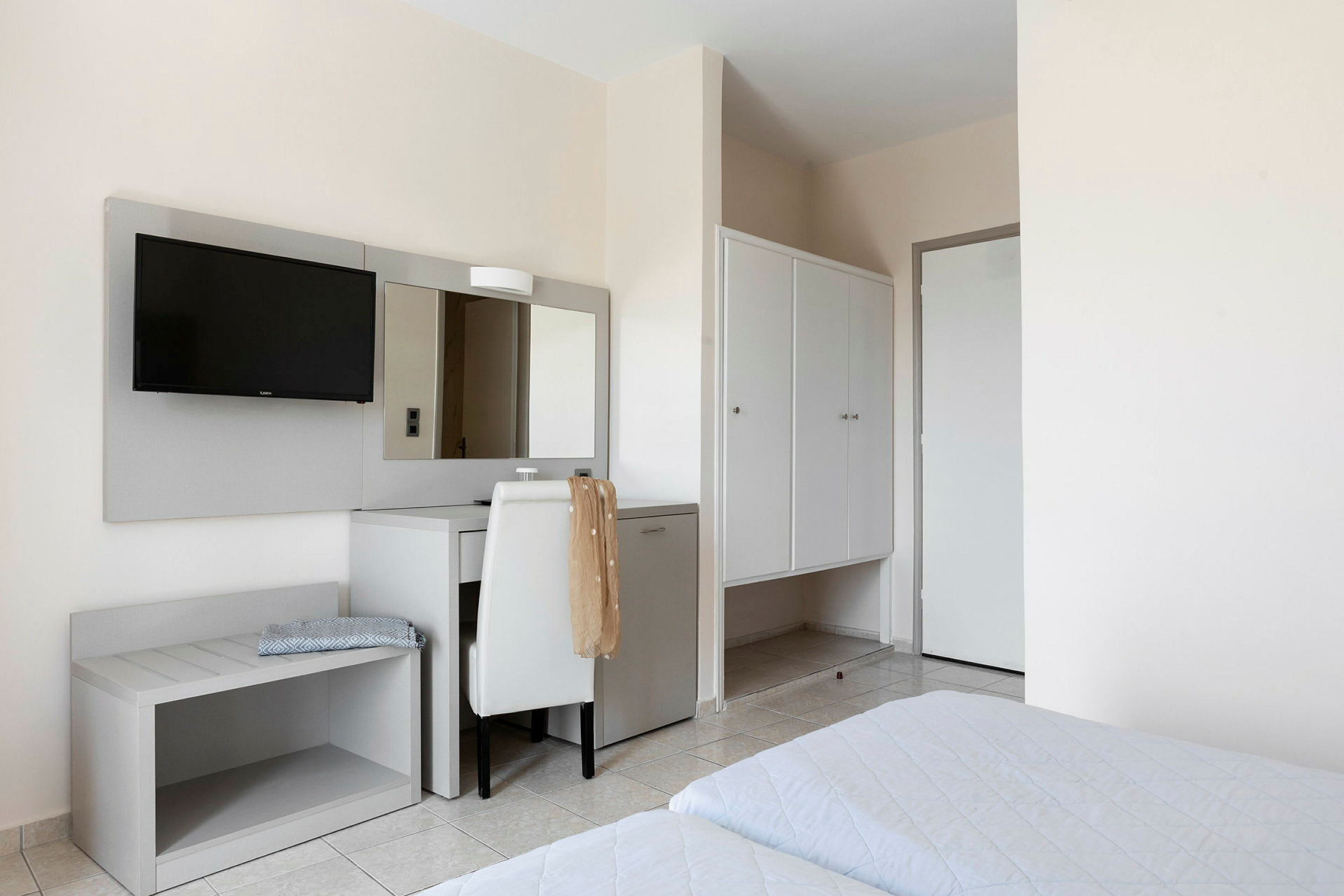 Hotelværelse med senge, skrivebord, spejl og garderobe. (AI-genereret tekst)