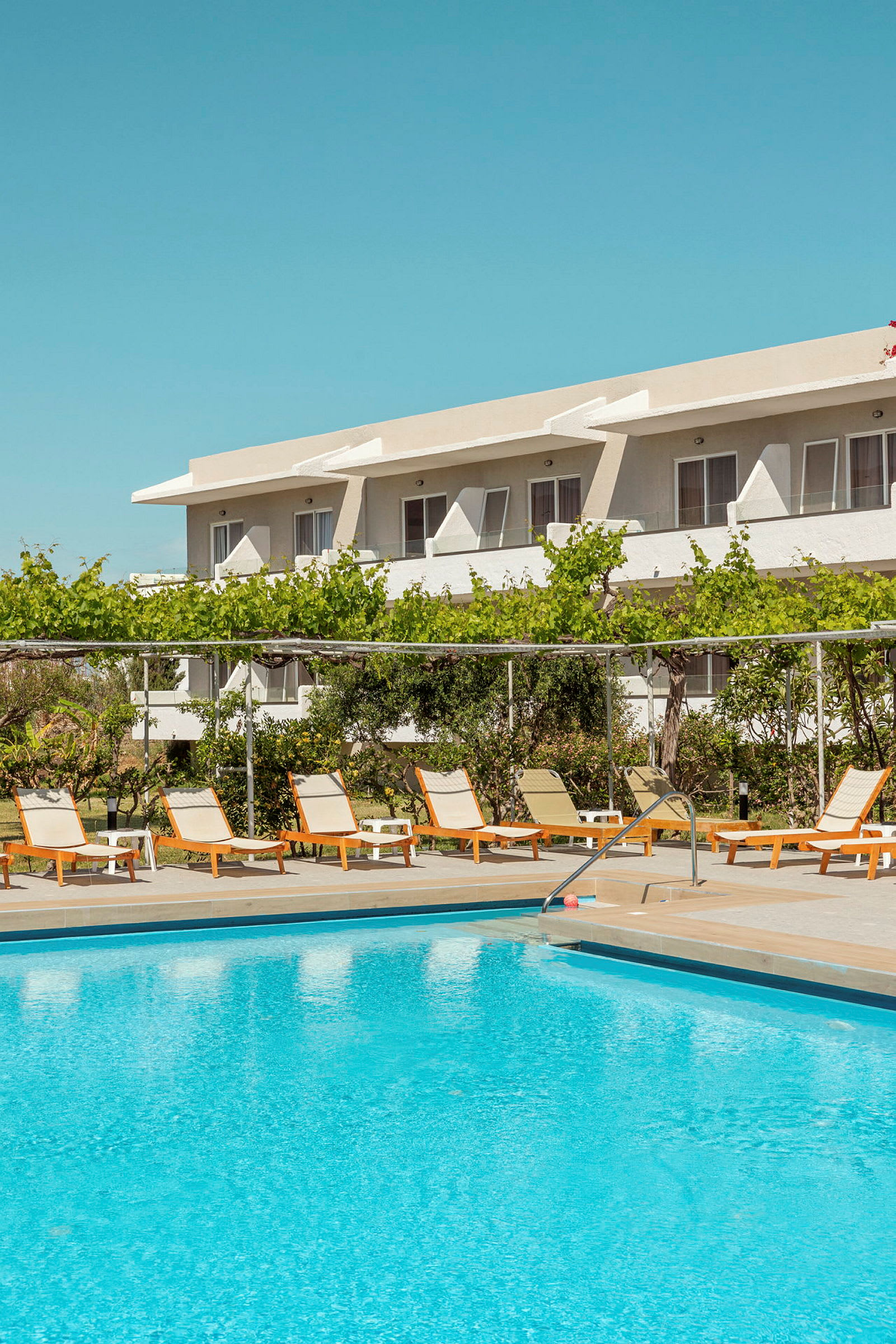 Udendørs swimmingpool med liggestole og afslapningsområde foran et hotel. (AI-genereret tekst)