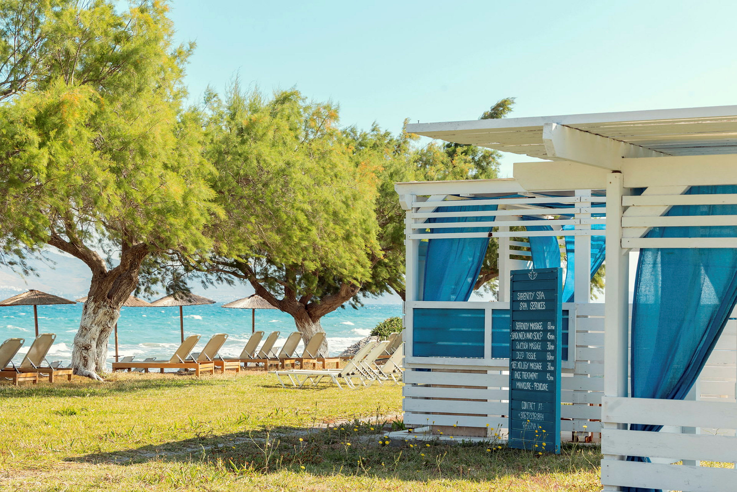 Et spa med blå gardiner ved en grøn strand med liggestole og parasoller. (AI-genereret tekst)