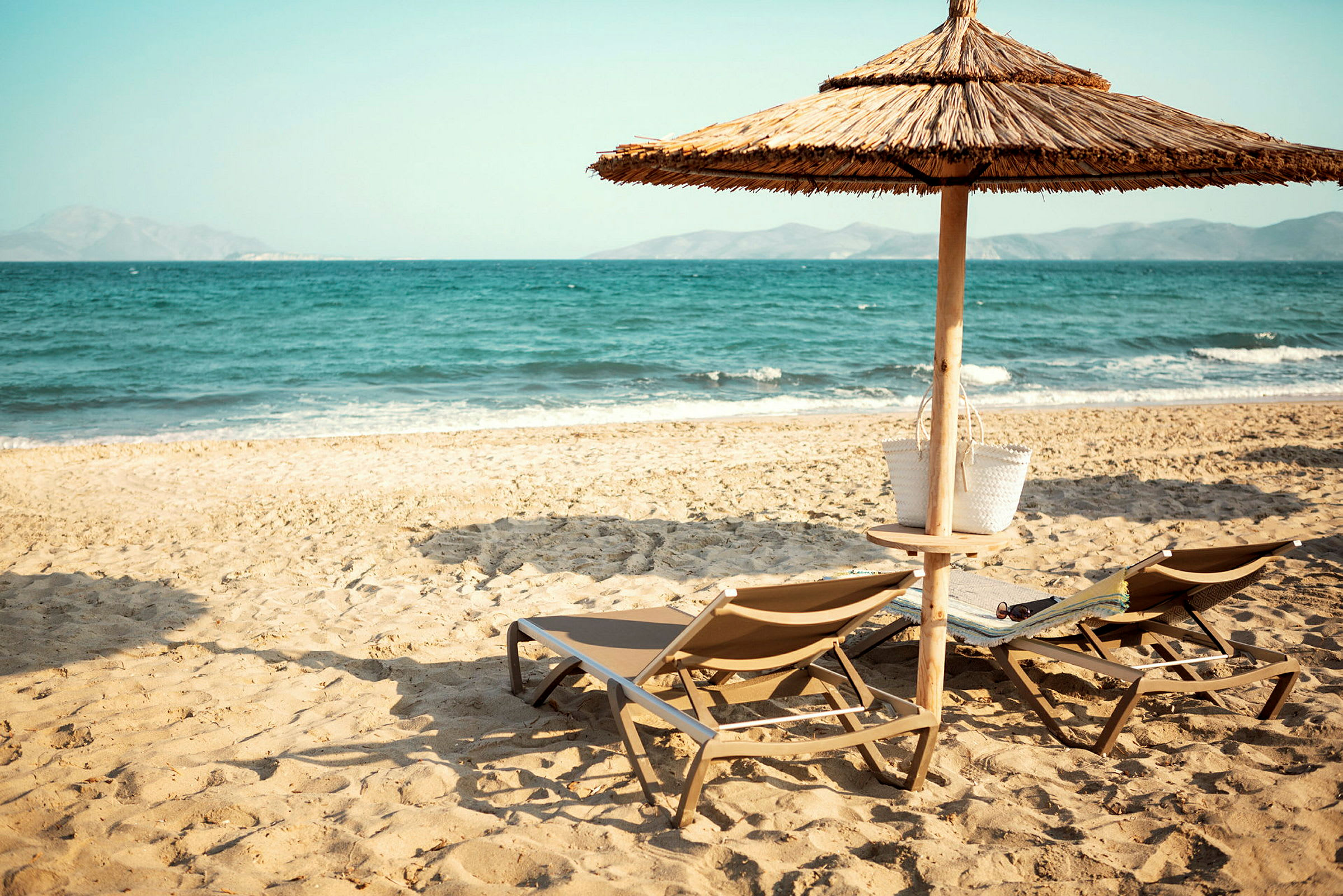 To solsenge og en parasol på en sandstrand ved havet. (AI-genereret tekst)