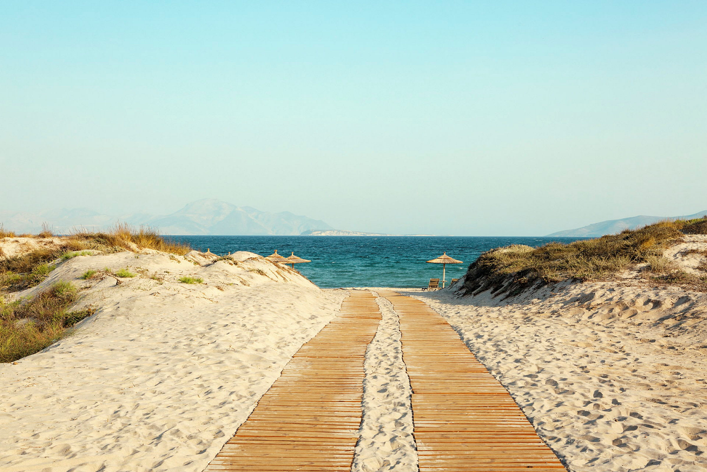 En træbro fører over en sandstrand til havet. (AI-genereret tekst)