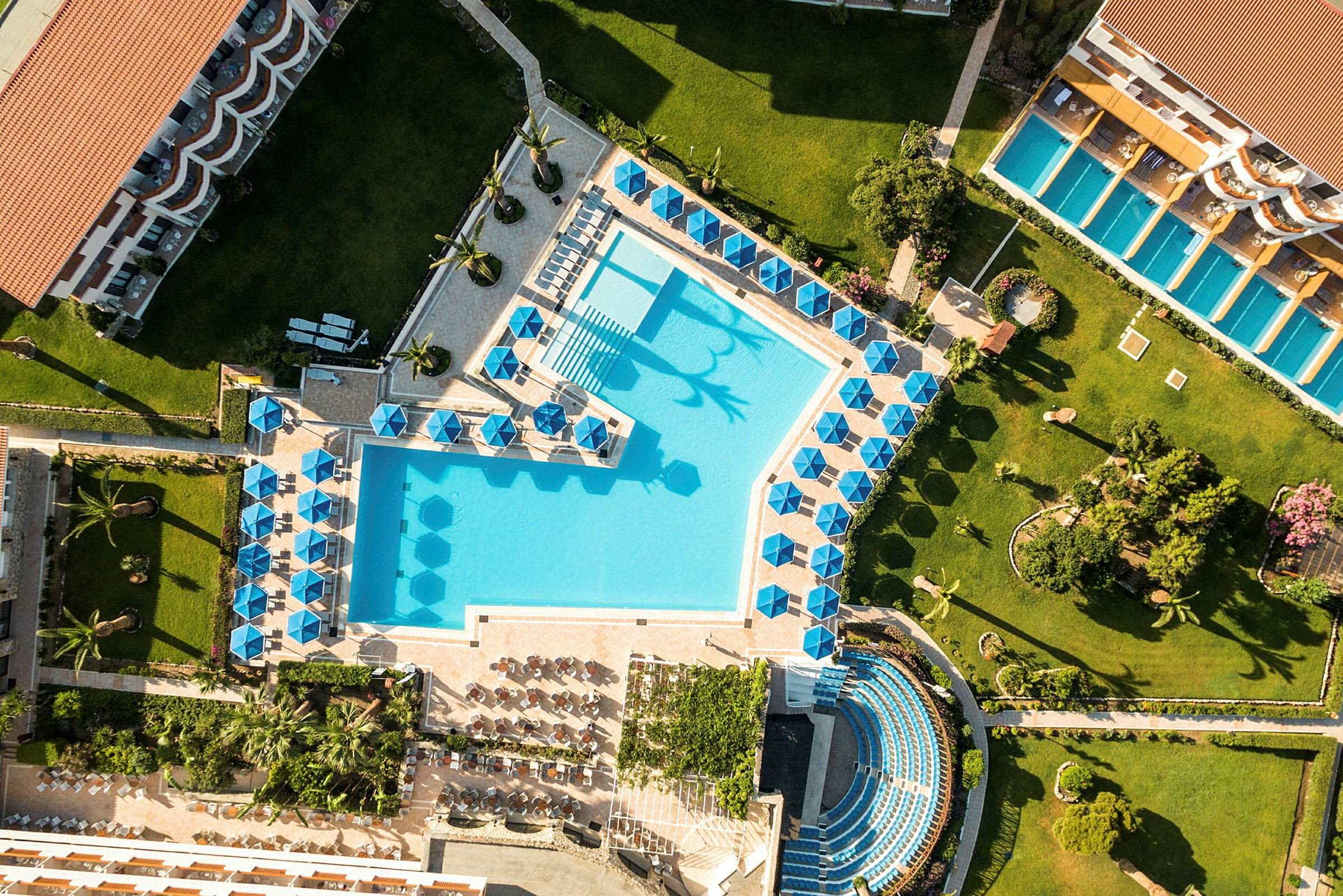 Luftfoto af et hotelområde med pool, liggestole og grønne områder. (AI-genereret tekst)