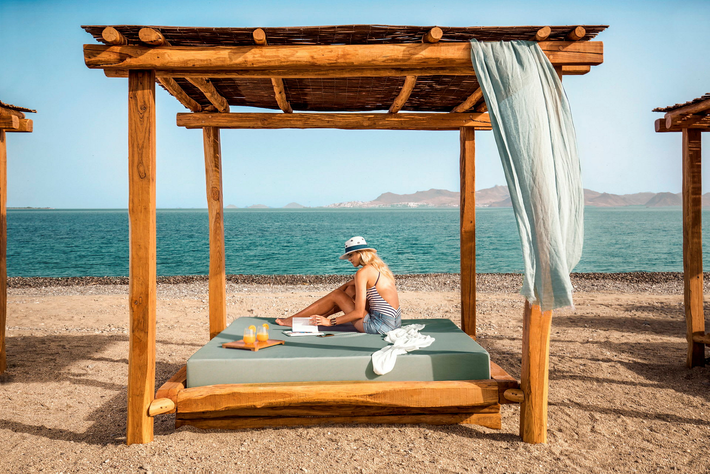 En person sidder under en træpergola på en strand med havet i baggrunden. (AI-genereret tekst)