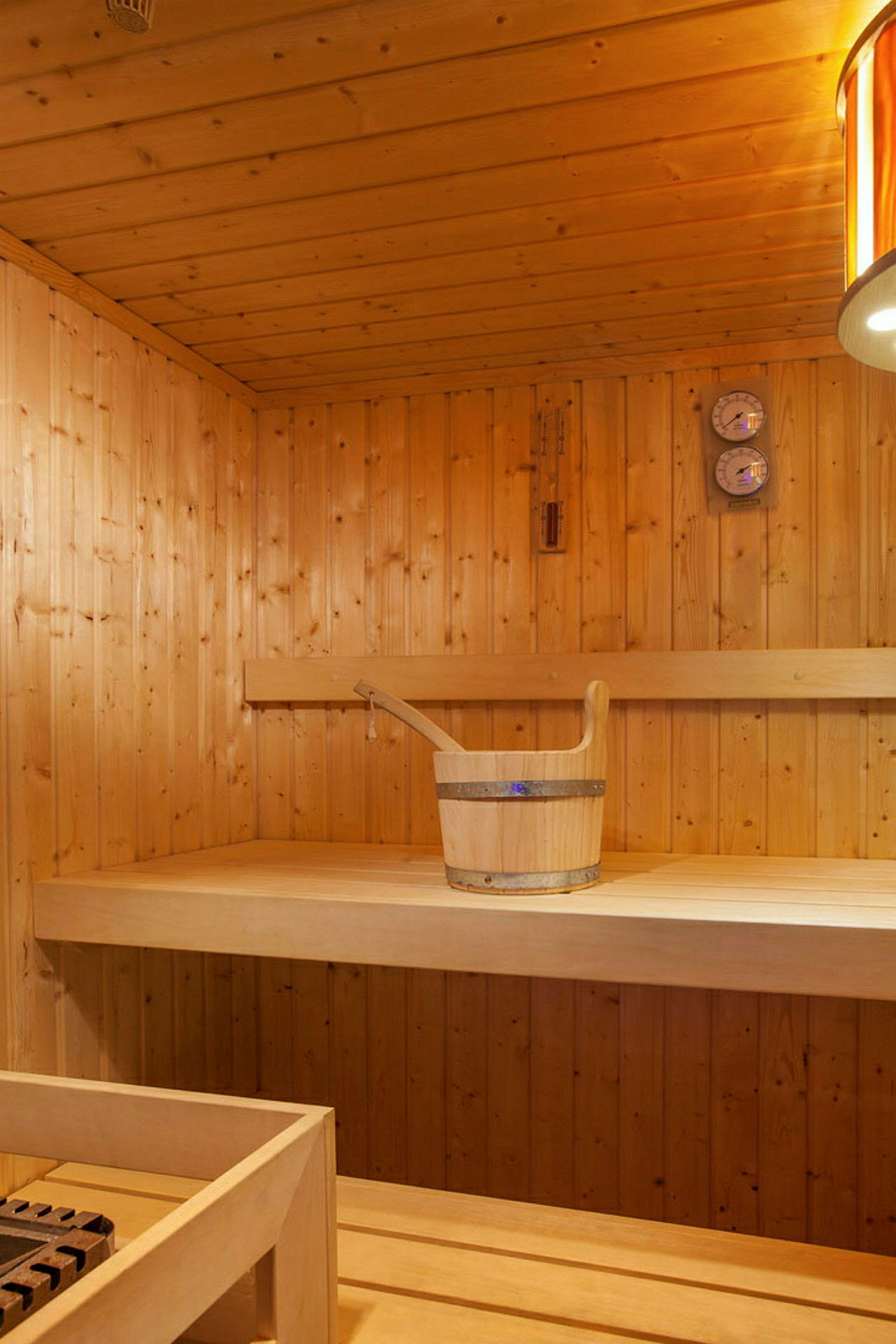 Interiør af en sauna med træpaneler og en spand på en bænk. (AI-genereret tekst)