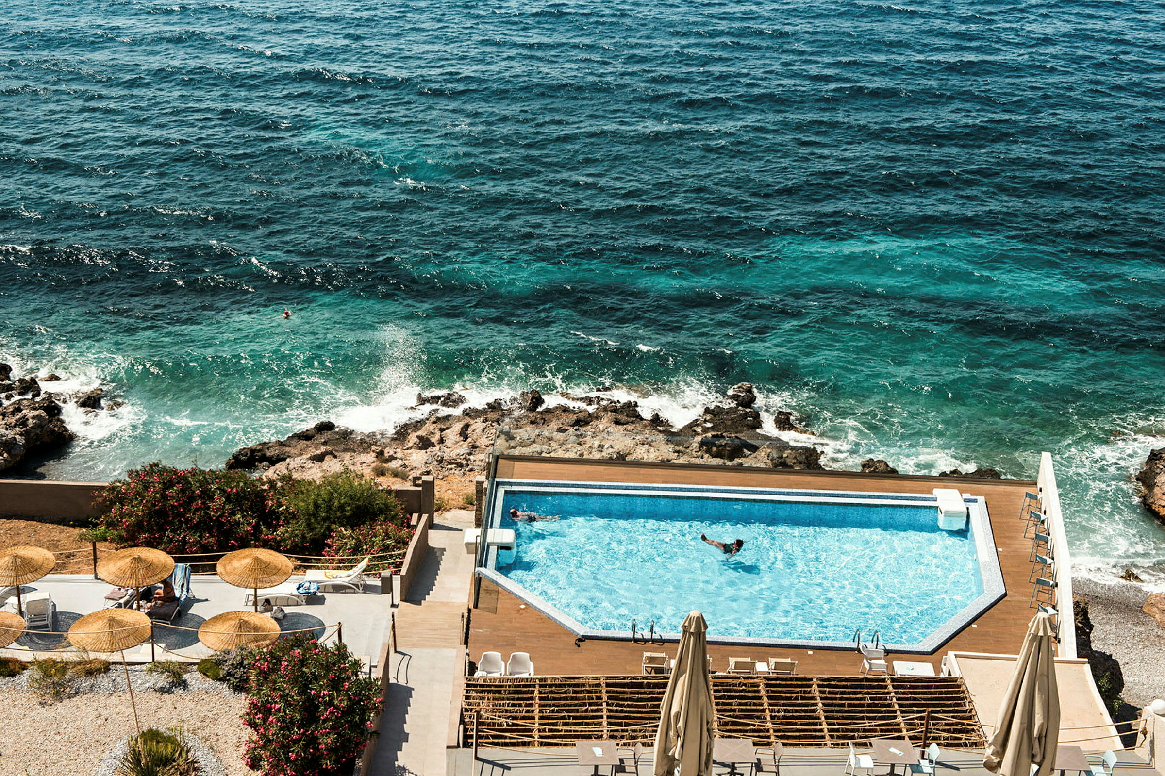 Udsigt over hotelpool ved havet med liggestole og parasoller. (AI-genereret tekst)