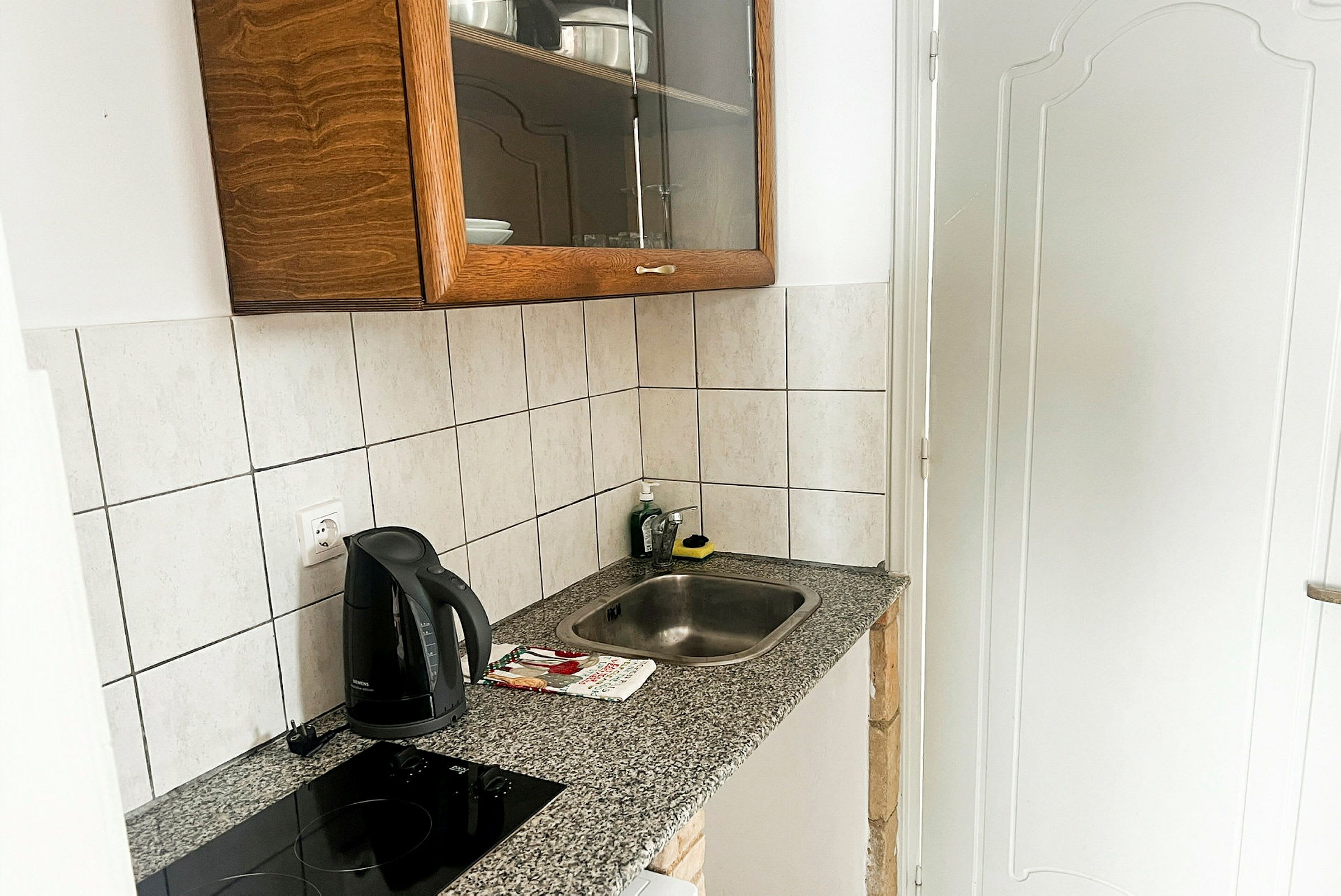Et lille køkken med en vask, en induktionskogeplade, en elkedel og et skab. (AI-genereret tekst)