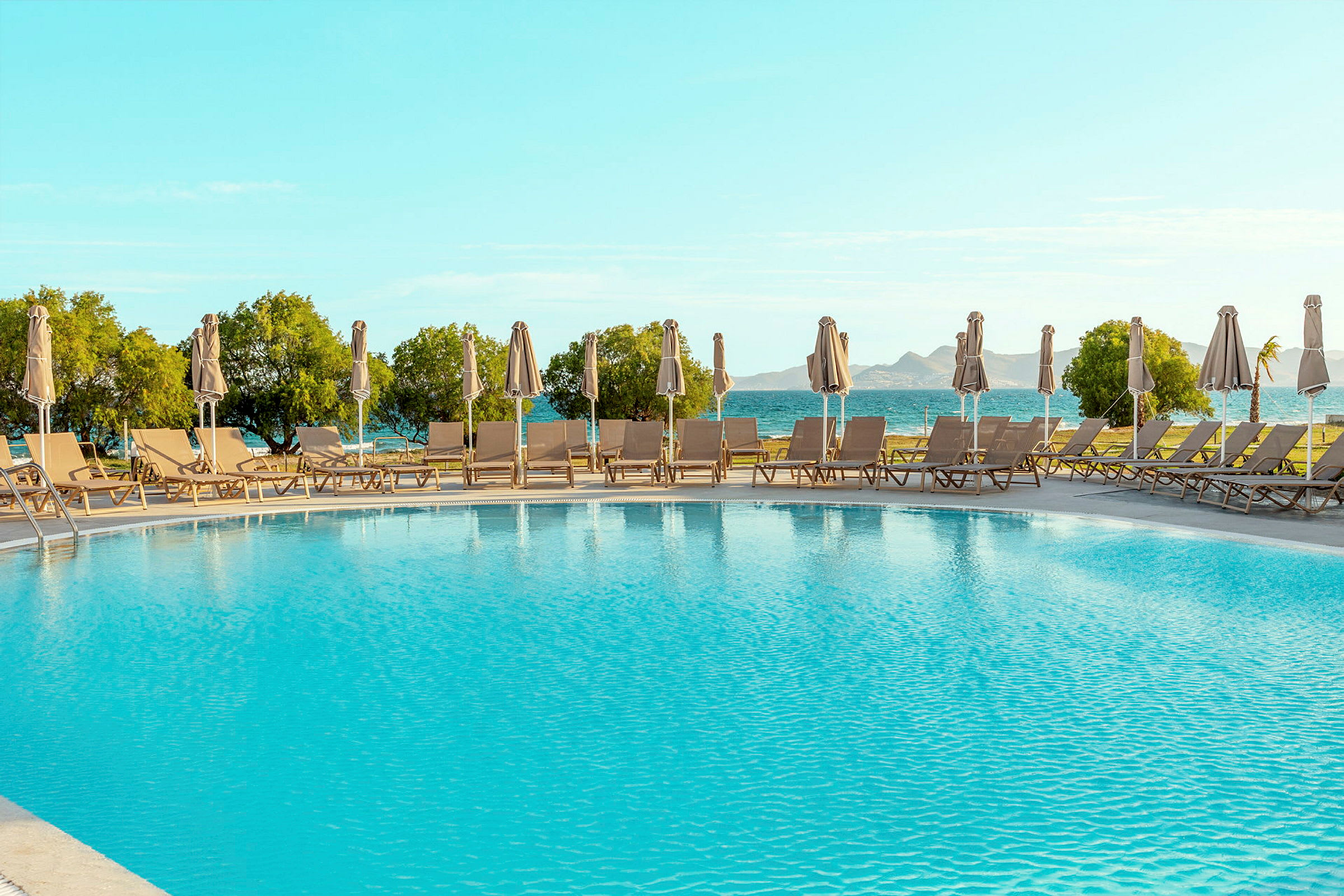Pool med liggestole og parasoller på en solrig dag. (AI-genereret tekst)