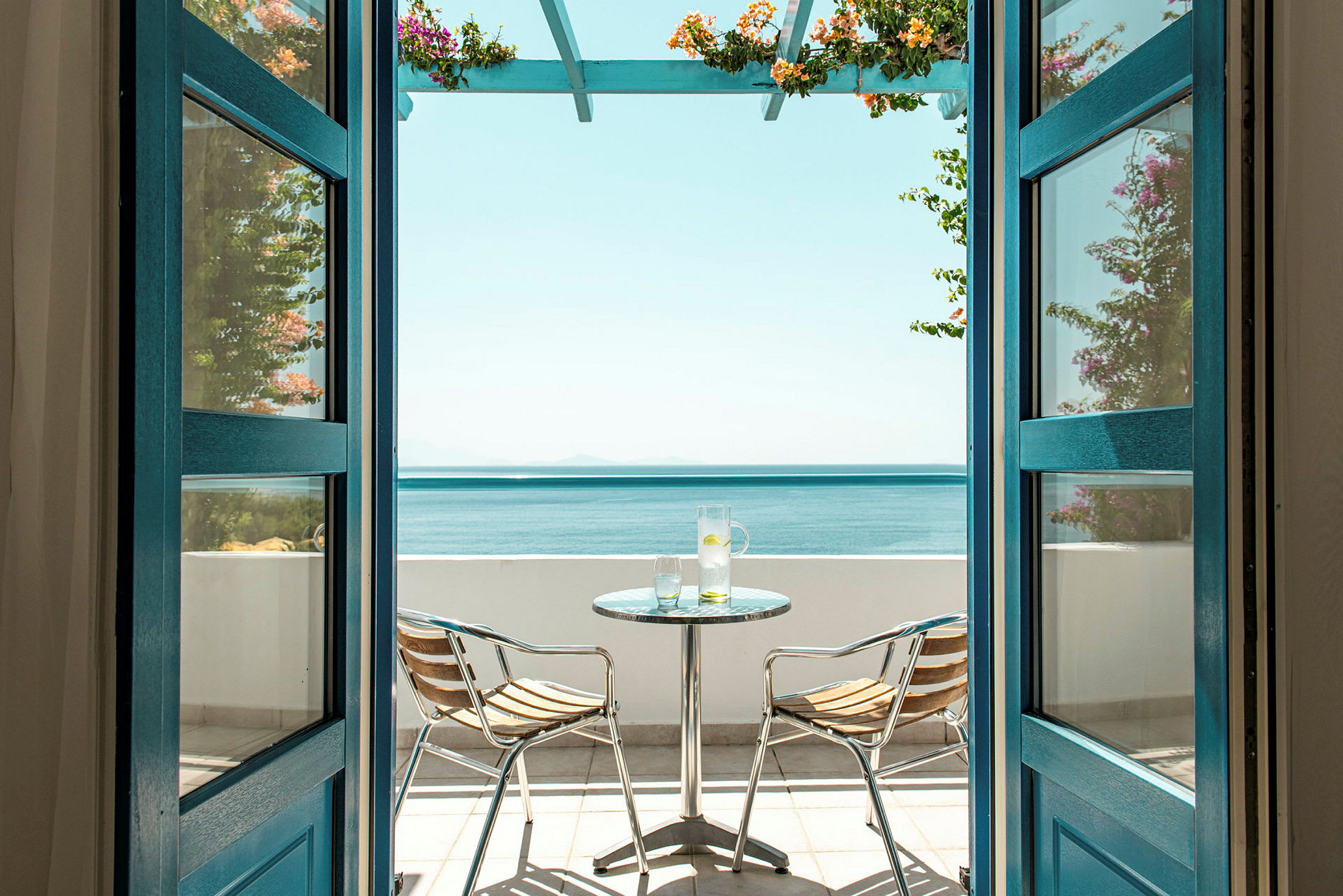 Udsigt gennem åbne døre til en terrasse med havudsigt, inklusive et bord og to stole. (AI-genereret tekst)