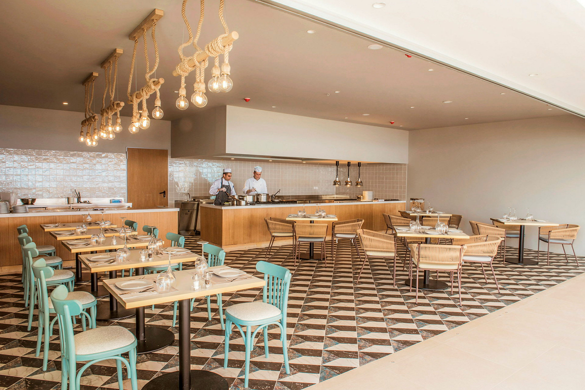 Moderne restaurantinteriør med træborde og turkise stole samt et åbent køkken med kokke. (AI-genereret tekst)