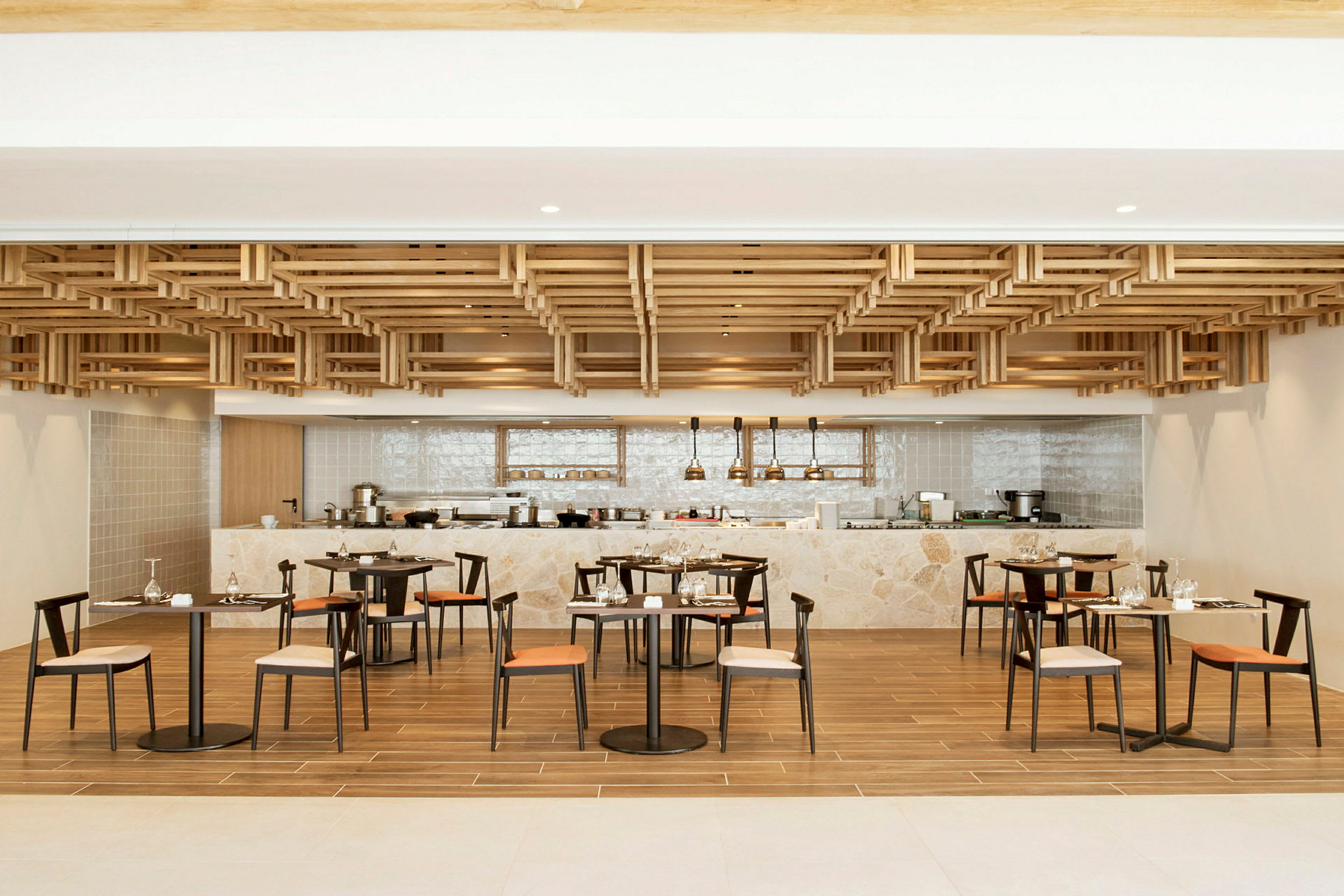 En moderne restaurant med trækonstruktioner i loftet, borde og stole samt en bardisk i baggrunden. (AI-genereret tekst)