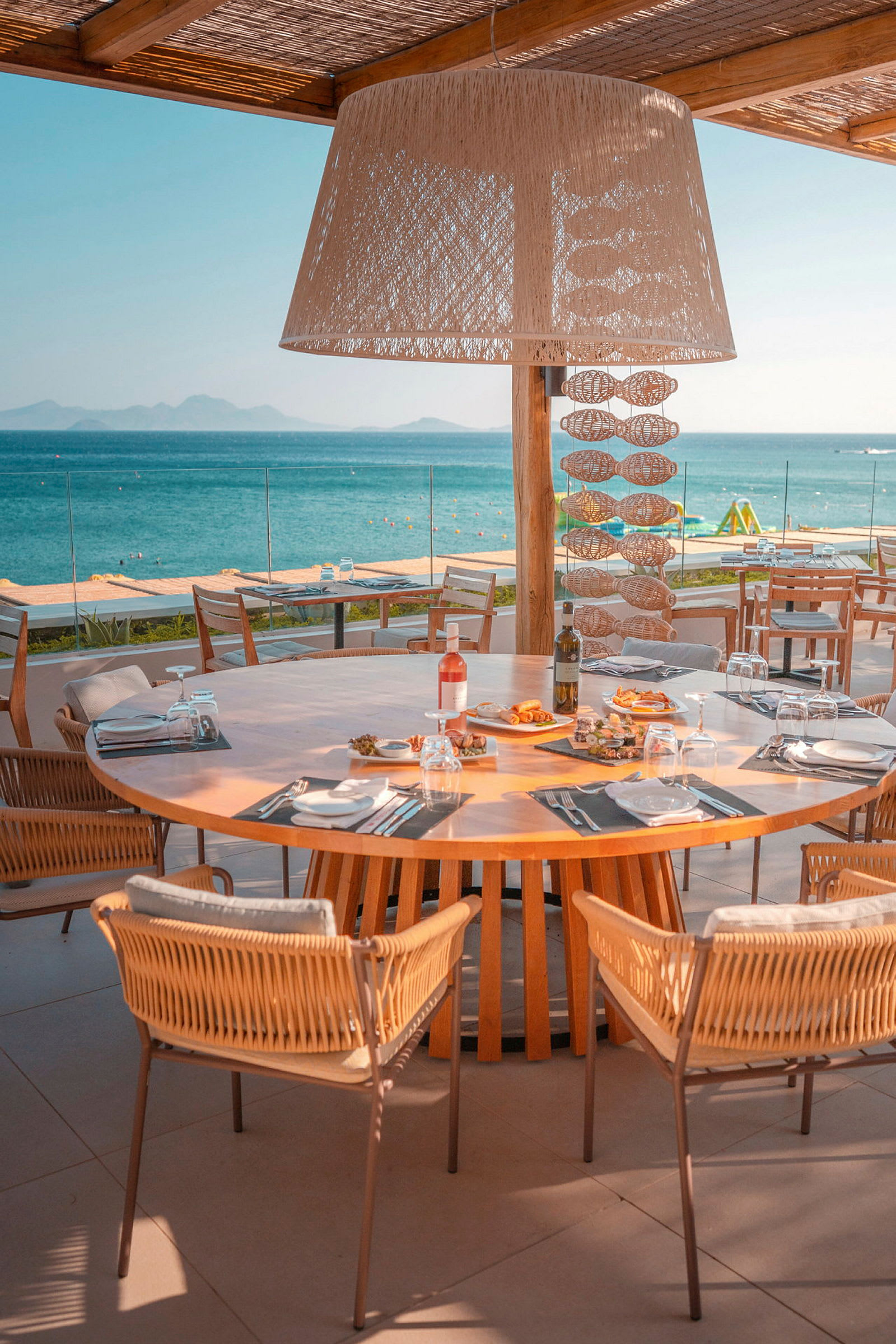 Et dækket træbord med stole på en restaurantterrasse ud mod havet. (AI-genereret tekst)