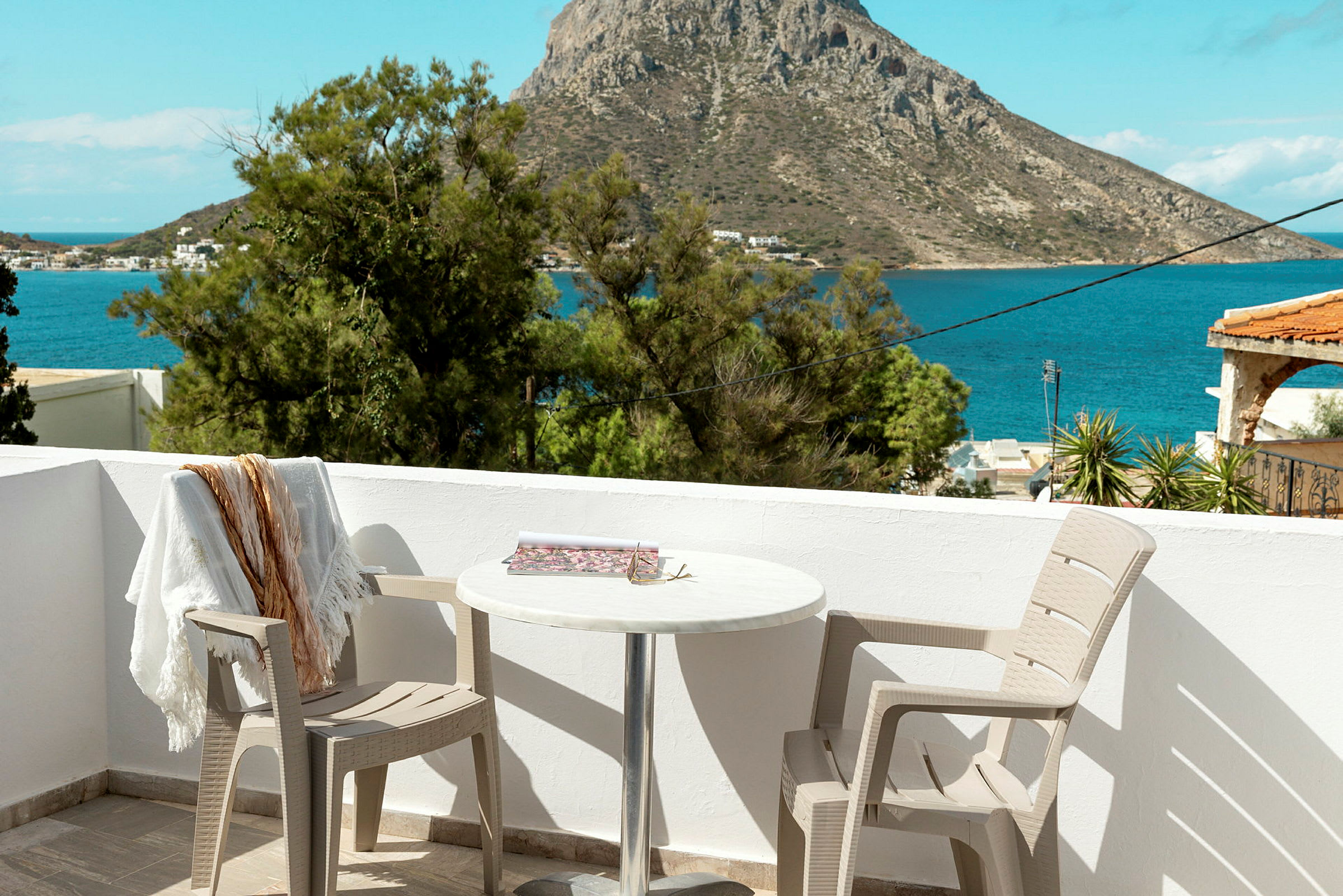 Udsigt fra en terrasse med to stole og et bord, mod havet og en klippe i baggrunden. (AI-genereret tekst)