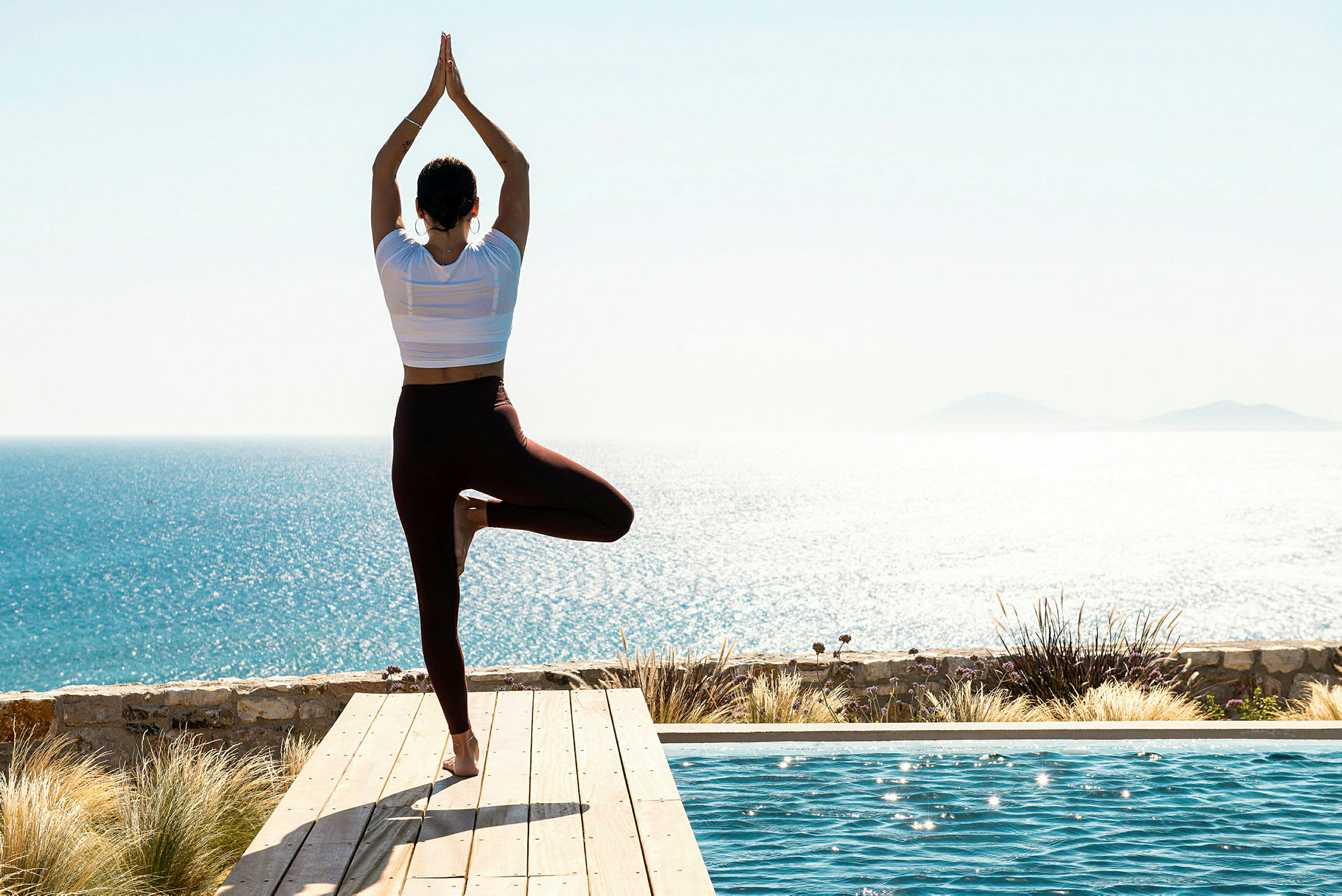Person, der laver yoga ved en pool med havudsigt. (AI-genereret tekst)