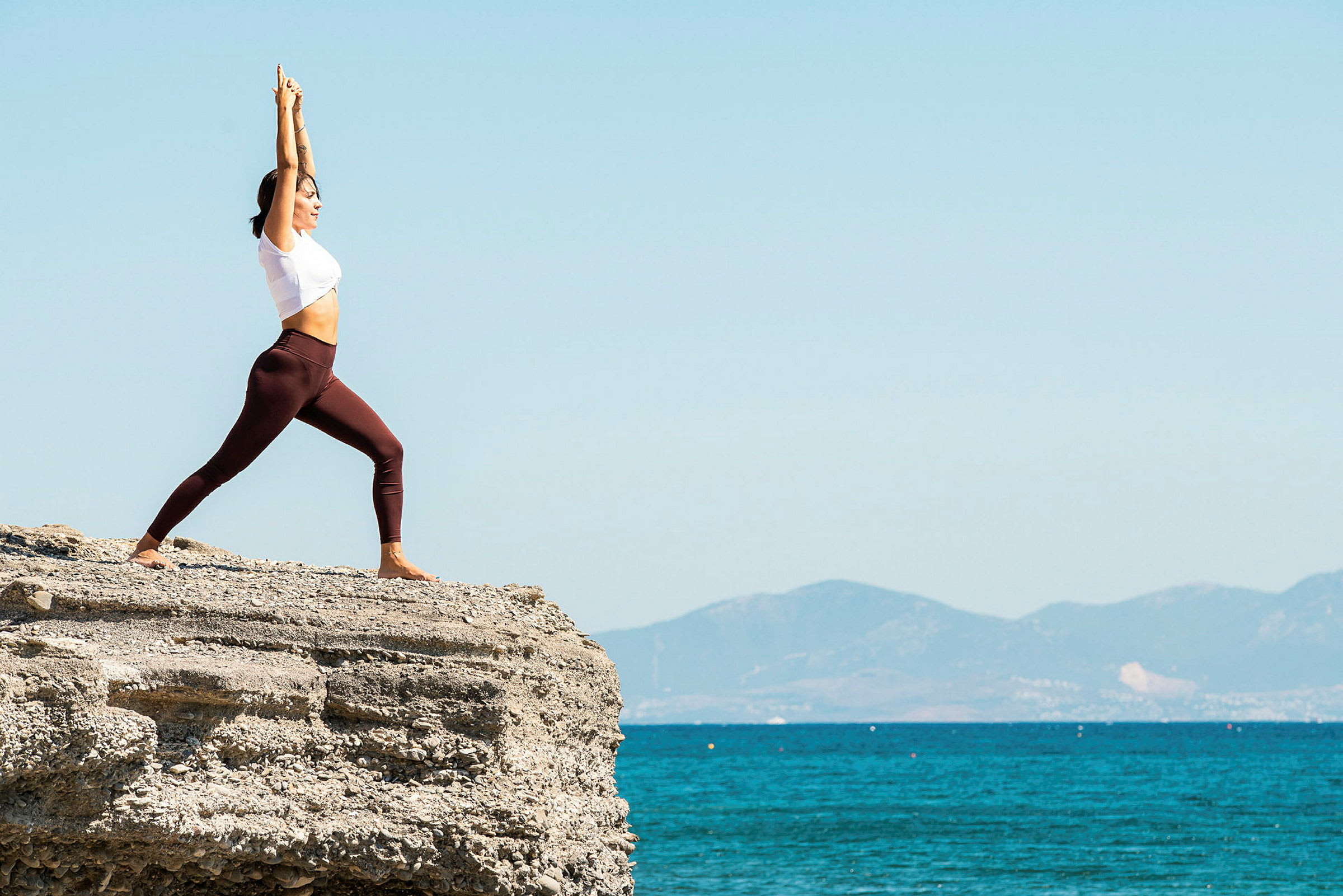 En person laver yoga på en klippe ved havet med bjerge i baggrunden. (AI-genereret tekst)