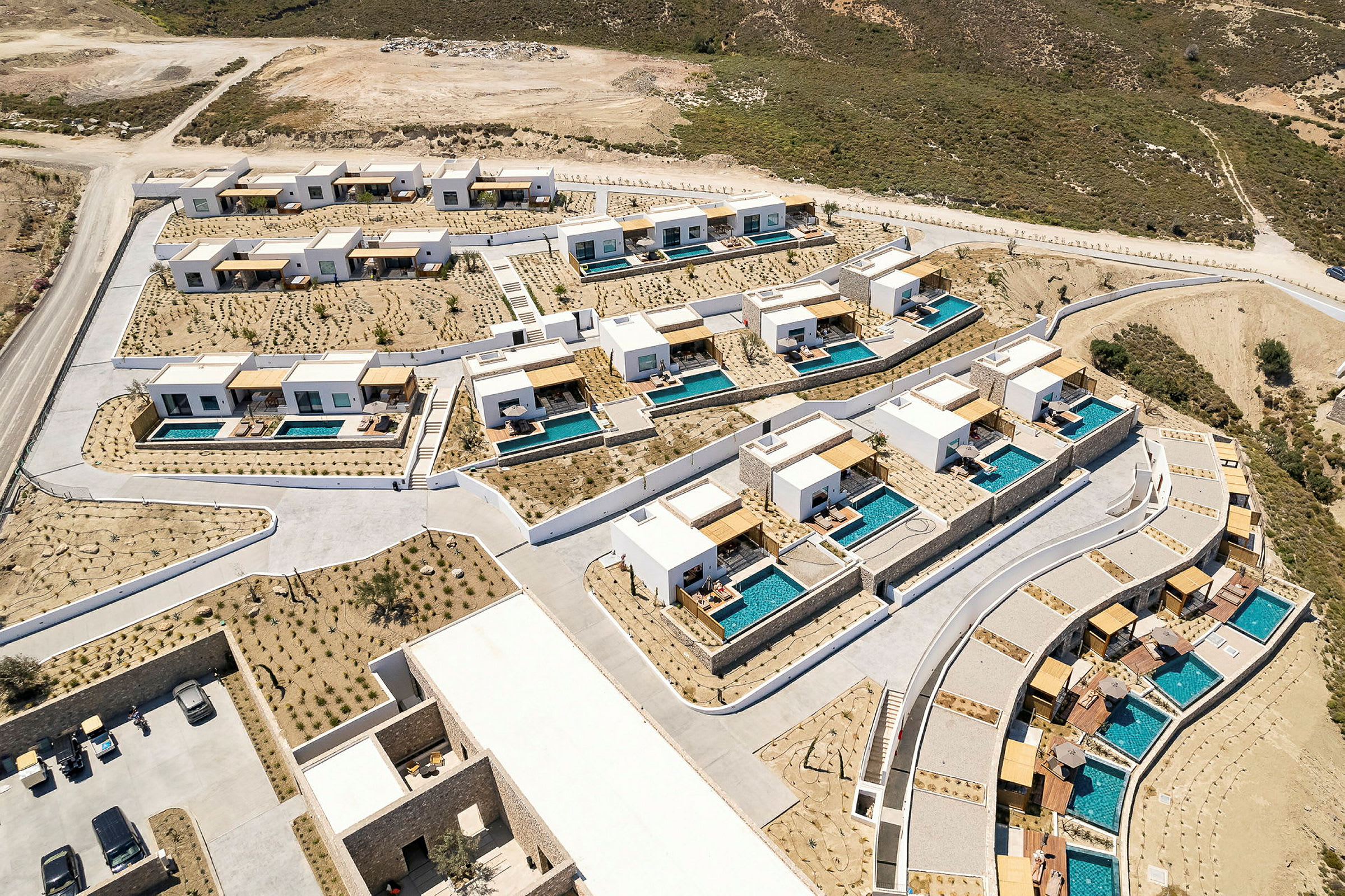 Luftfoto af et resort med moderne huse og private pools omgivet af tørt landskab. (AI-genereret tekst)
