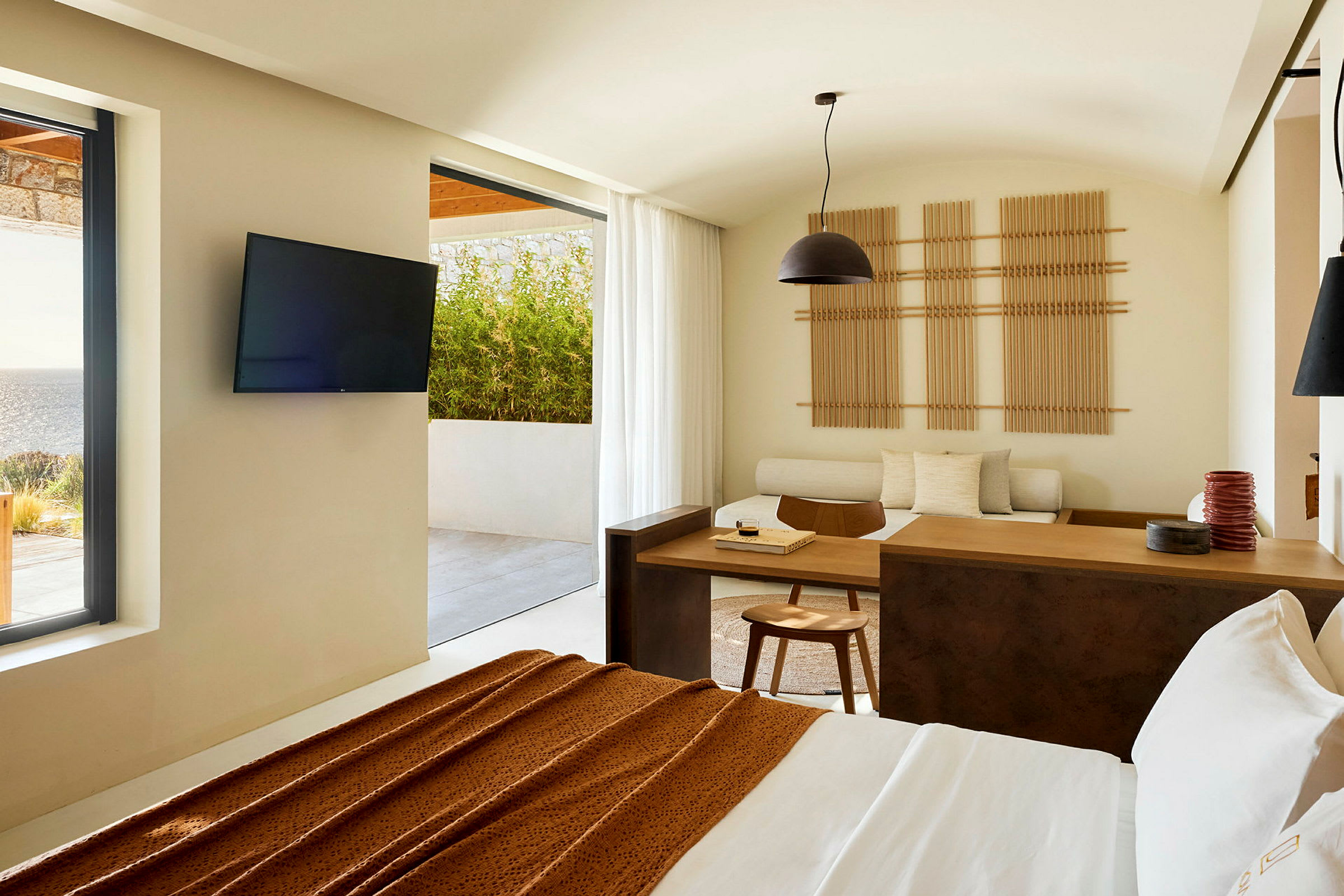 Et moderne hotelværelse med udsigt til en terrasse og havet, indrettet med minimalistiske møbler og lyse farver. (AI-genereret tekst)