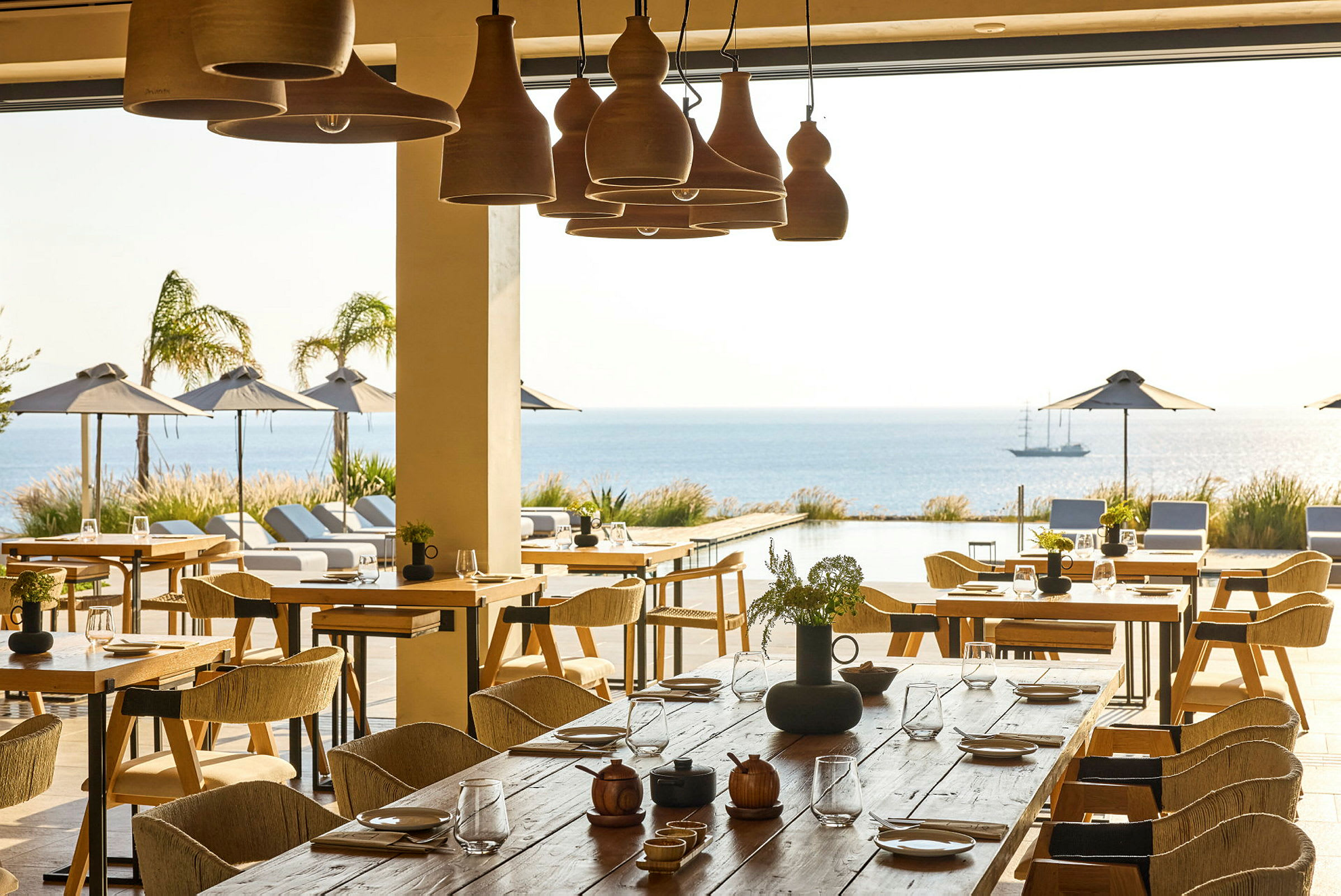 En restaurant med borde og stole, med udsigt over en udendørs pool, havet og parasoller. (AI-genereret tekst)