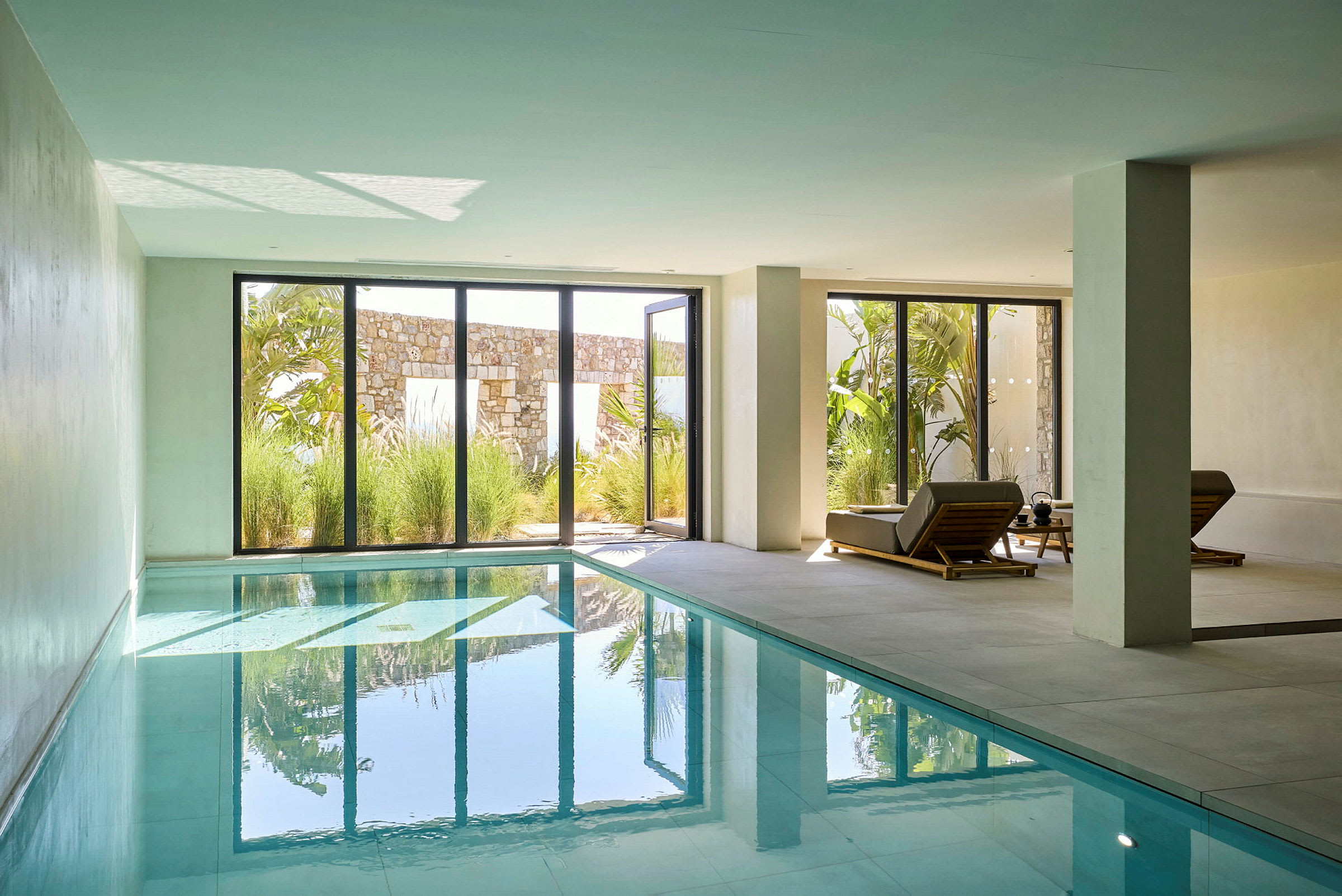 Indendørs swimmingpool med udsigt til en have gennem store glasvinduer. (AI-genereret tekst)