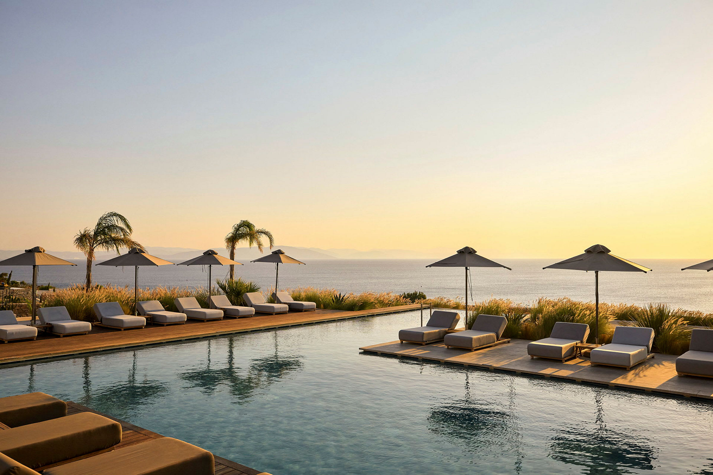 En infinitypool omgivet af liggestole og parasoller ved solnedgang, med udsigt over havet. (AI-genereret tekst)