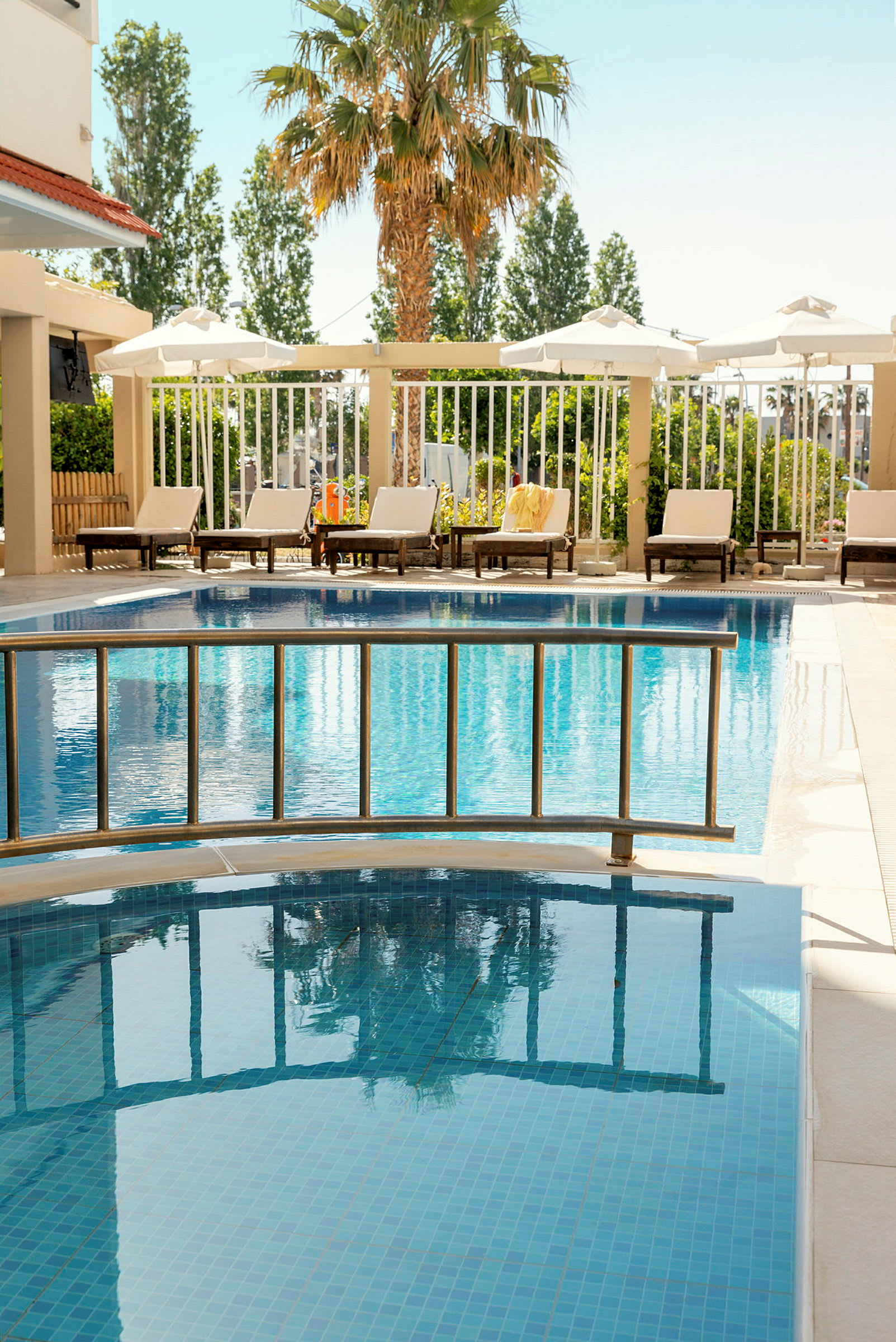 Hotelpool med liggestole og en palme i baggrunden. (AI-genereret tekst)