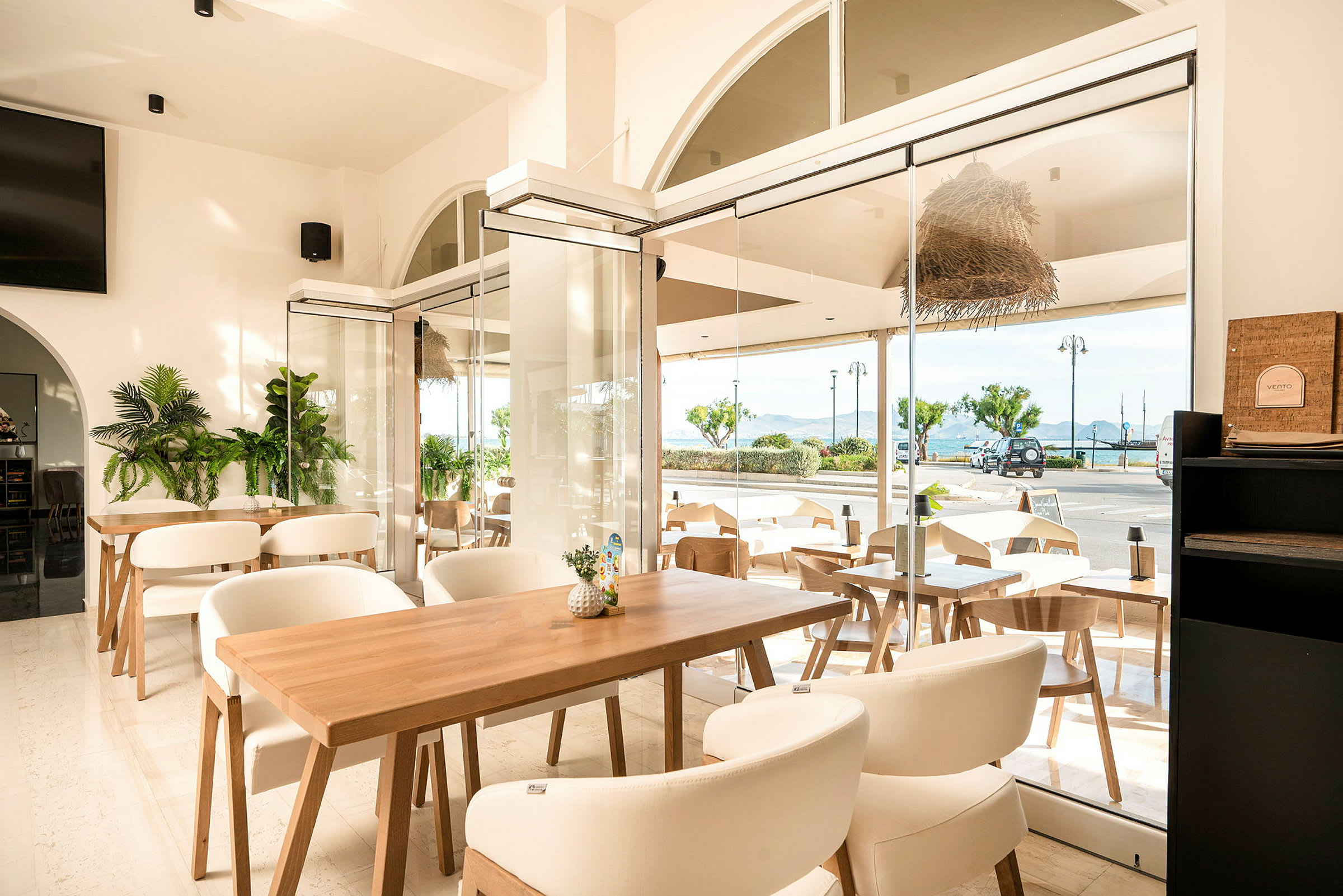 En lys og moderne indrettet café med store vinduer ud mod en gade og havudsigt. (AI-genereret tekst)