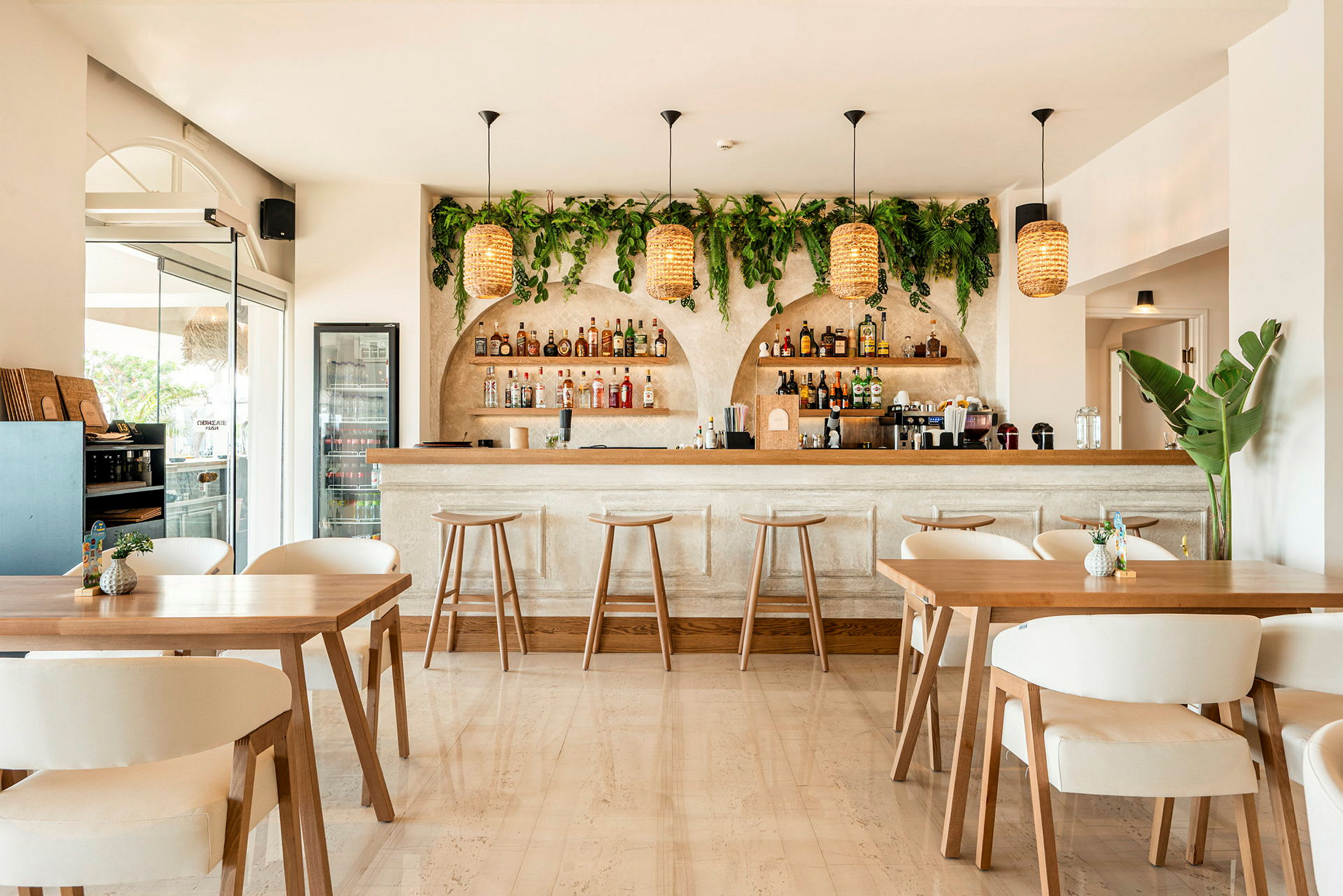 Billede af en stilren bar med lyst interiør. Baren har omkransende grøn planteudsmykning samt hængende flettede lamper. (AI-genereret tekst)
