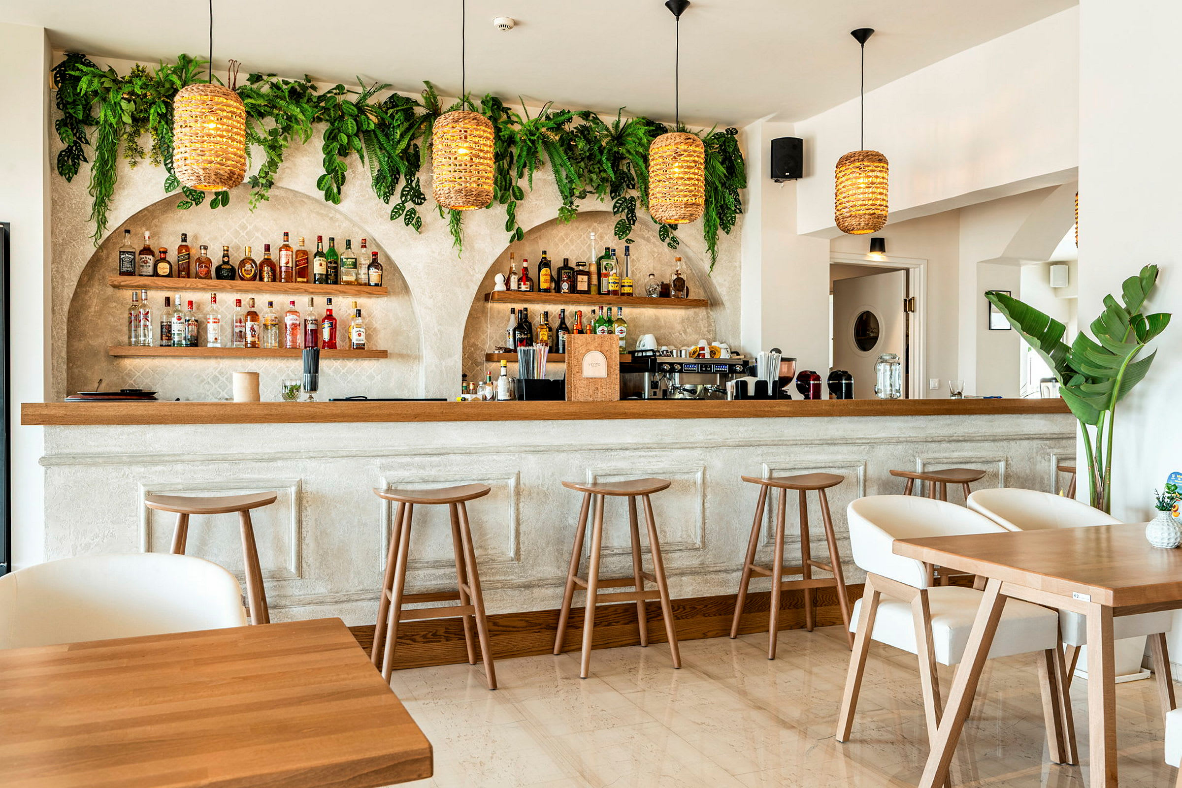 Et indendørsbillede af en moderne bar med træstole, borde og grønne planter på væggene. (AI-genereret tekst)