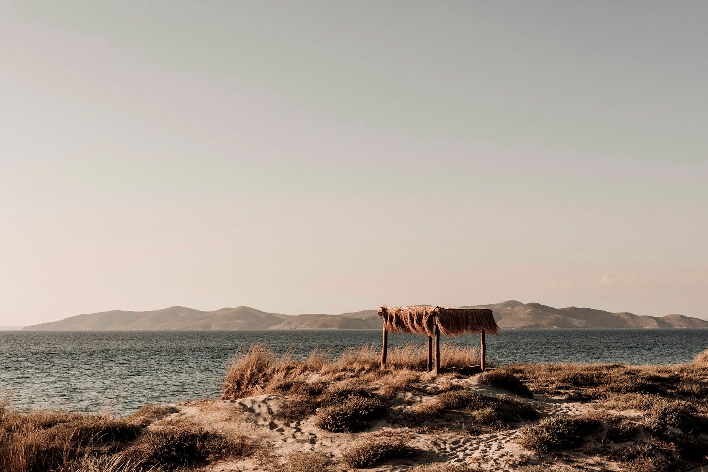 Et strandlandskab med et enkelt ly af træ og halm ved havet. (AI-genereret tekst)