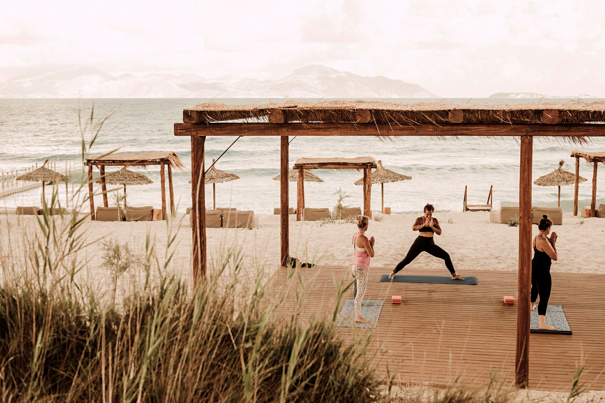 Personer udfører yoga på en strand med udsigt over havet og parasoller. (AI-genereret tekst)