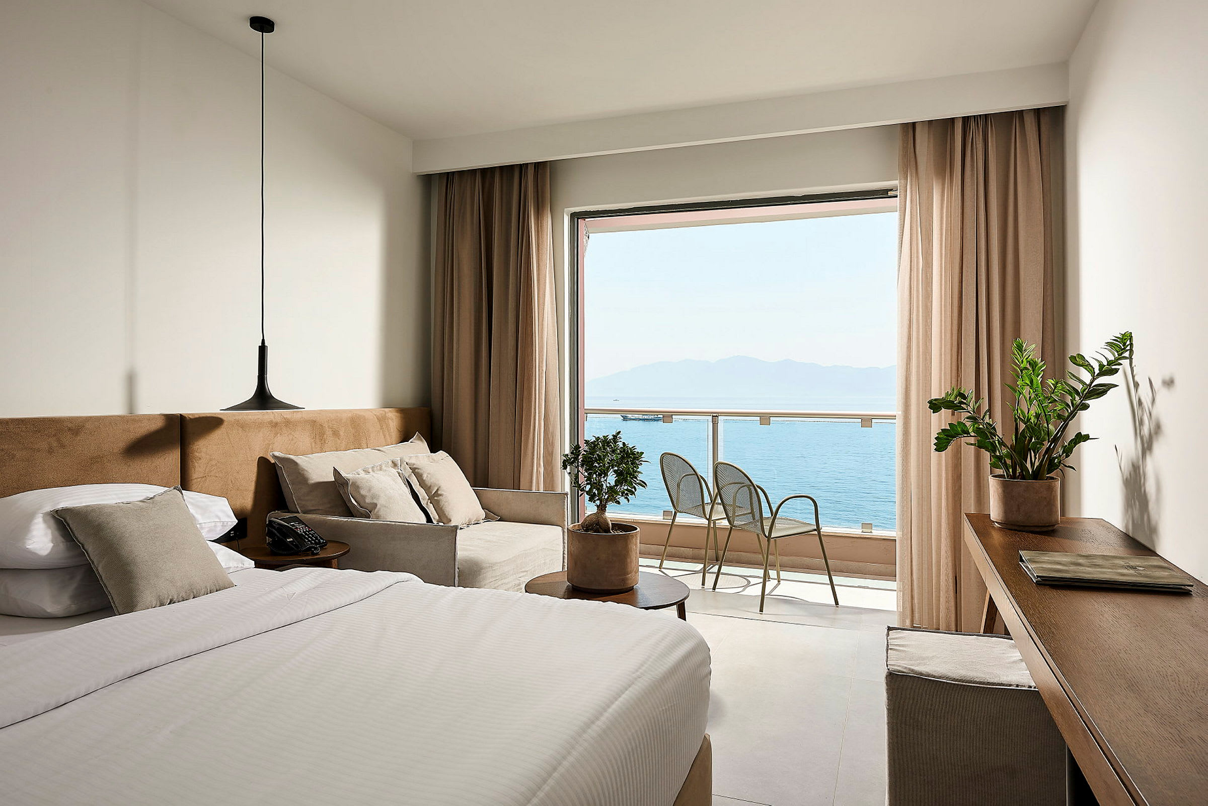 Et hotelværelse med en seng, sofa og udsigt over havet fra en balkon. (AI-genereret tekst)