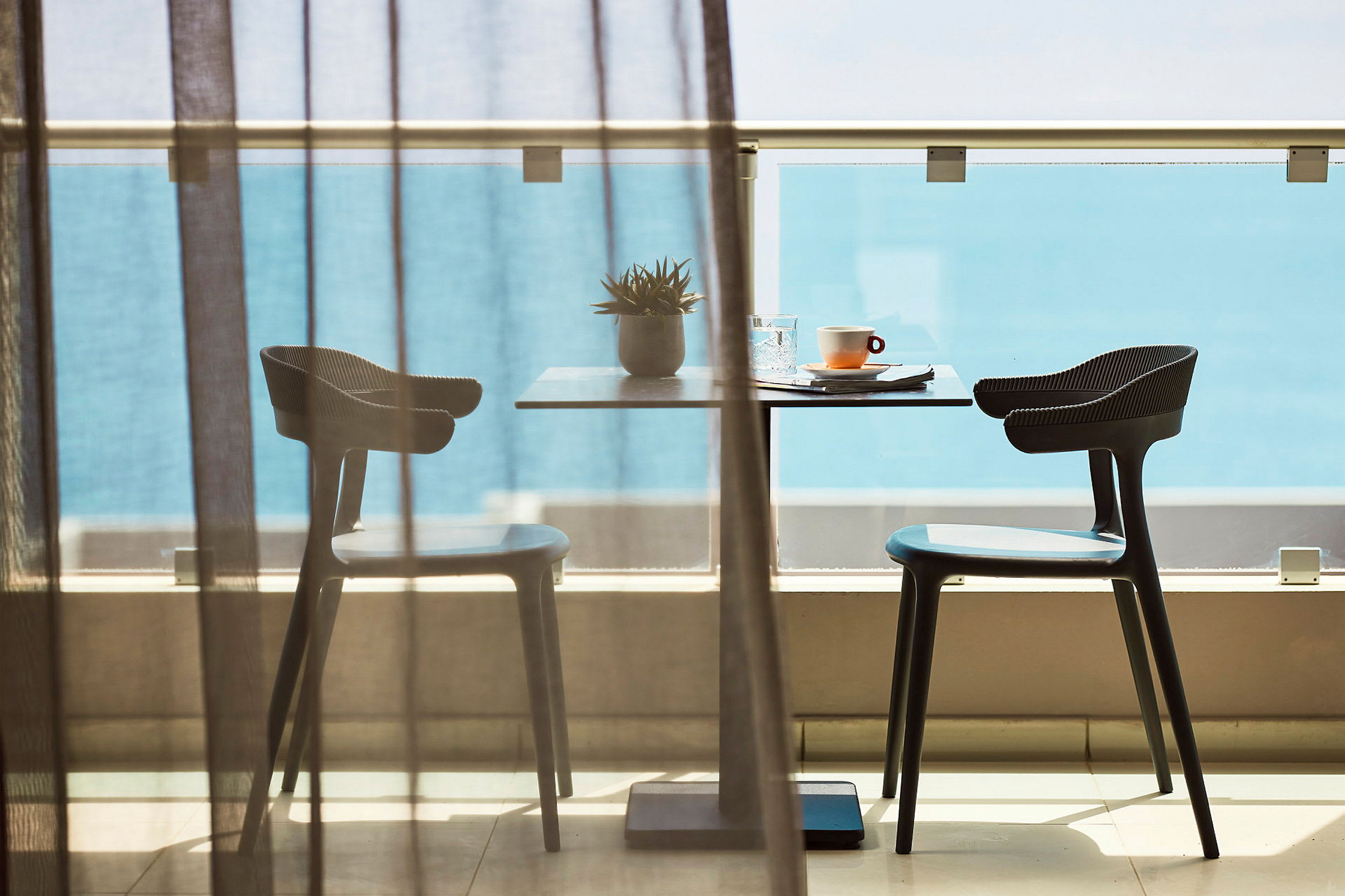 Et bord med to stole på en balkon foran havudsigt. (AI-genereret tekst)