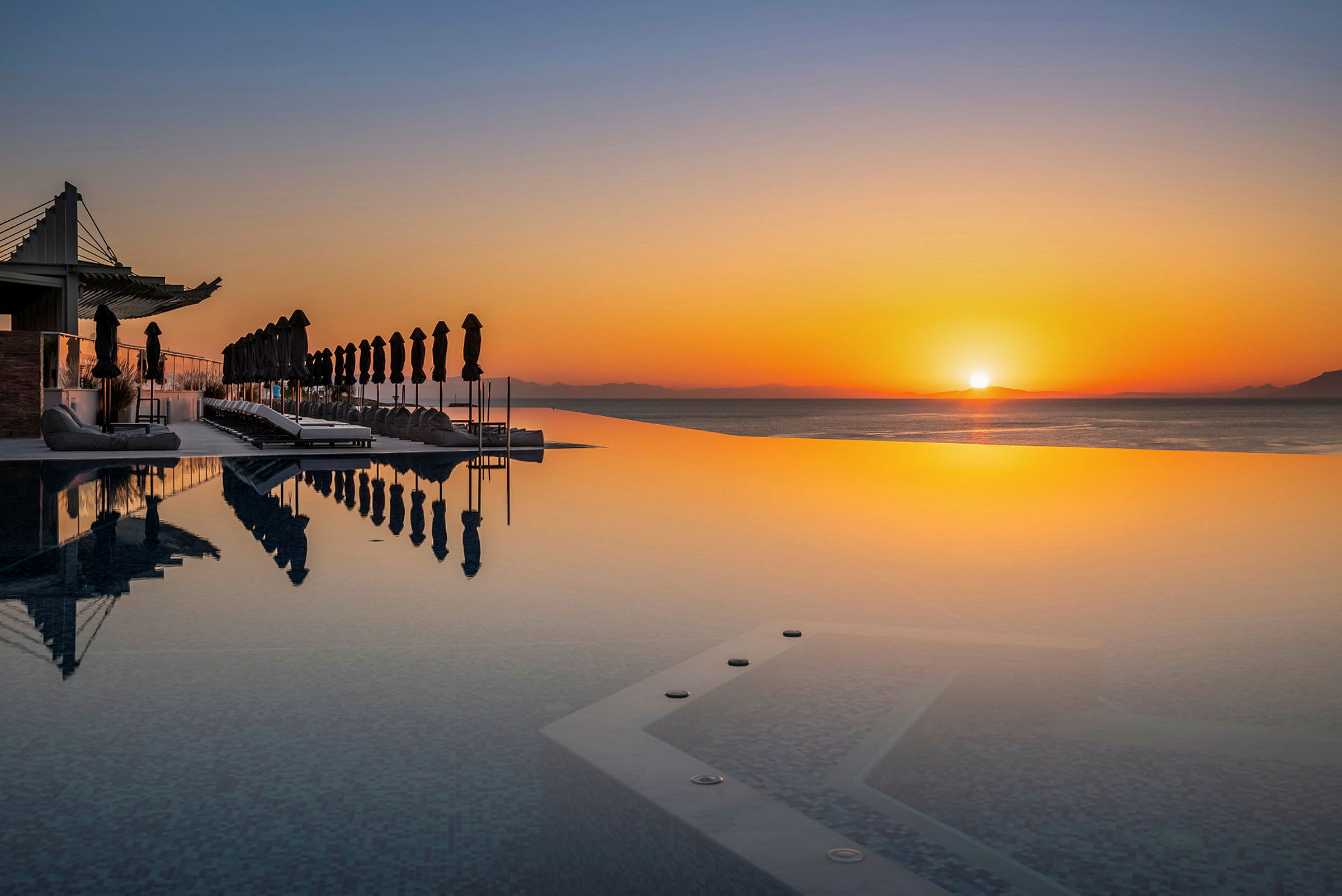 En infinitypool med liggestole og parasoller ved solnedgang. (AI-genereret tekst)
